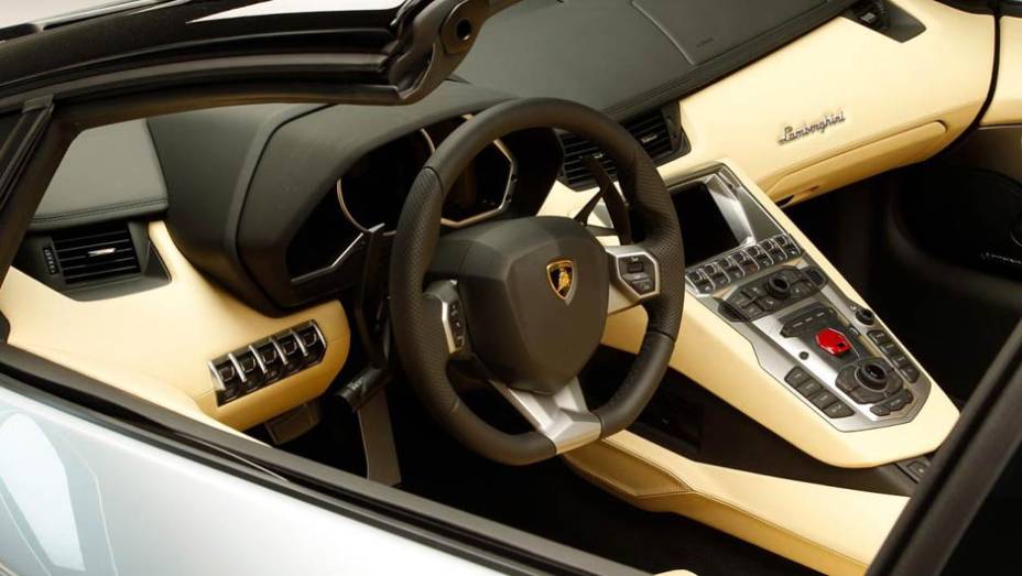 Moderno, o interior tem volante com base achatada e um envolvente console central | <a href="https://quatrorodas.abril.com.br/saloes/los-angeles/2012/lamborghini-aventador-roadster-lp700-4-724245.shtml" rel="migration">Leia mais</a>