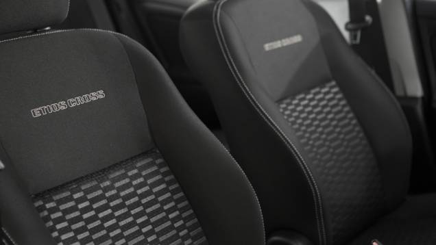 O revestimento Sport Comfort nos bancos ganhou costura branca e apresenta o nome do veículo gravado em alto relevo no encosto dos assentos dianteiros | <a href="https://quatrorodas.abril.com.br/carros/lancamentos/toyota-etios-cross-759424.shtml" rel="migration"></a>