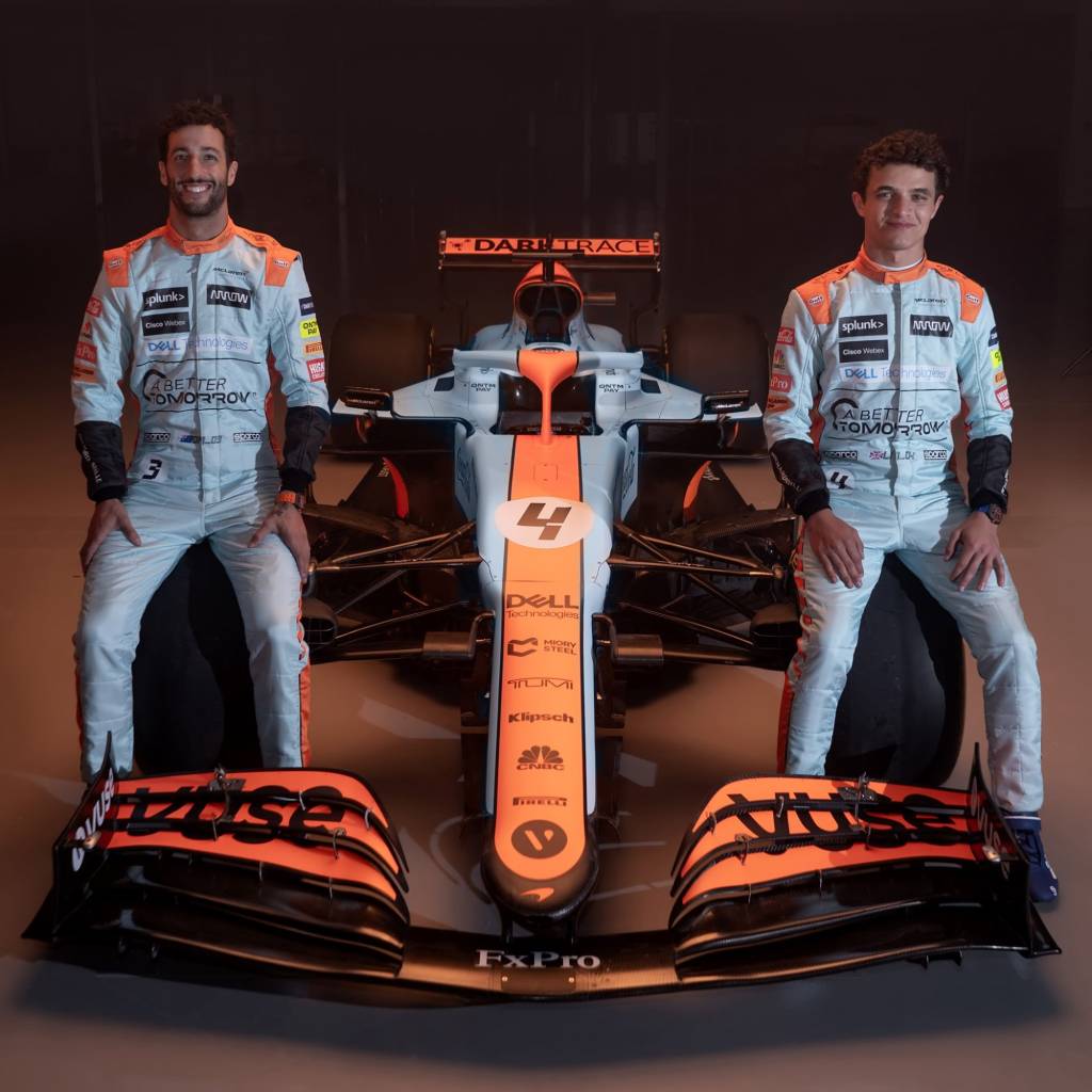 Daniel Ricciardo e Lando Norris sentados no carro de Fórmula 1 da McLaren visto de frente
