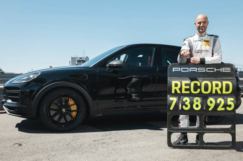 Porsche Cayenne Coupé Turbo preto visto de lado com piloto de teste segurando placa