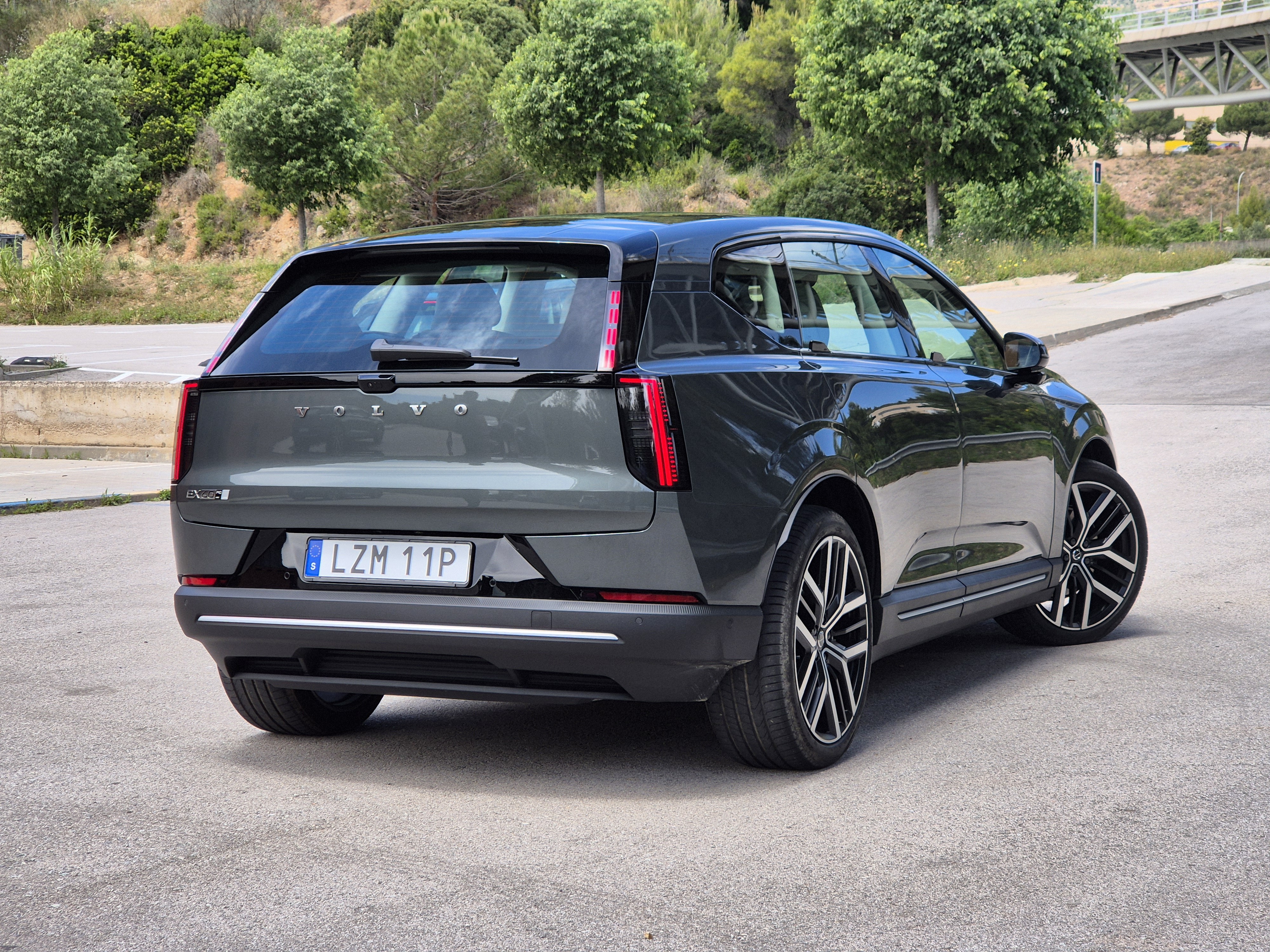 SUV Volvo EX60 cinza-escuro estacionado em uma rua asfaltada, visto por trás e lateralmente. As lanternas traseiras verticais e a placa