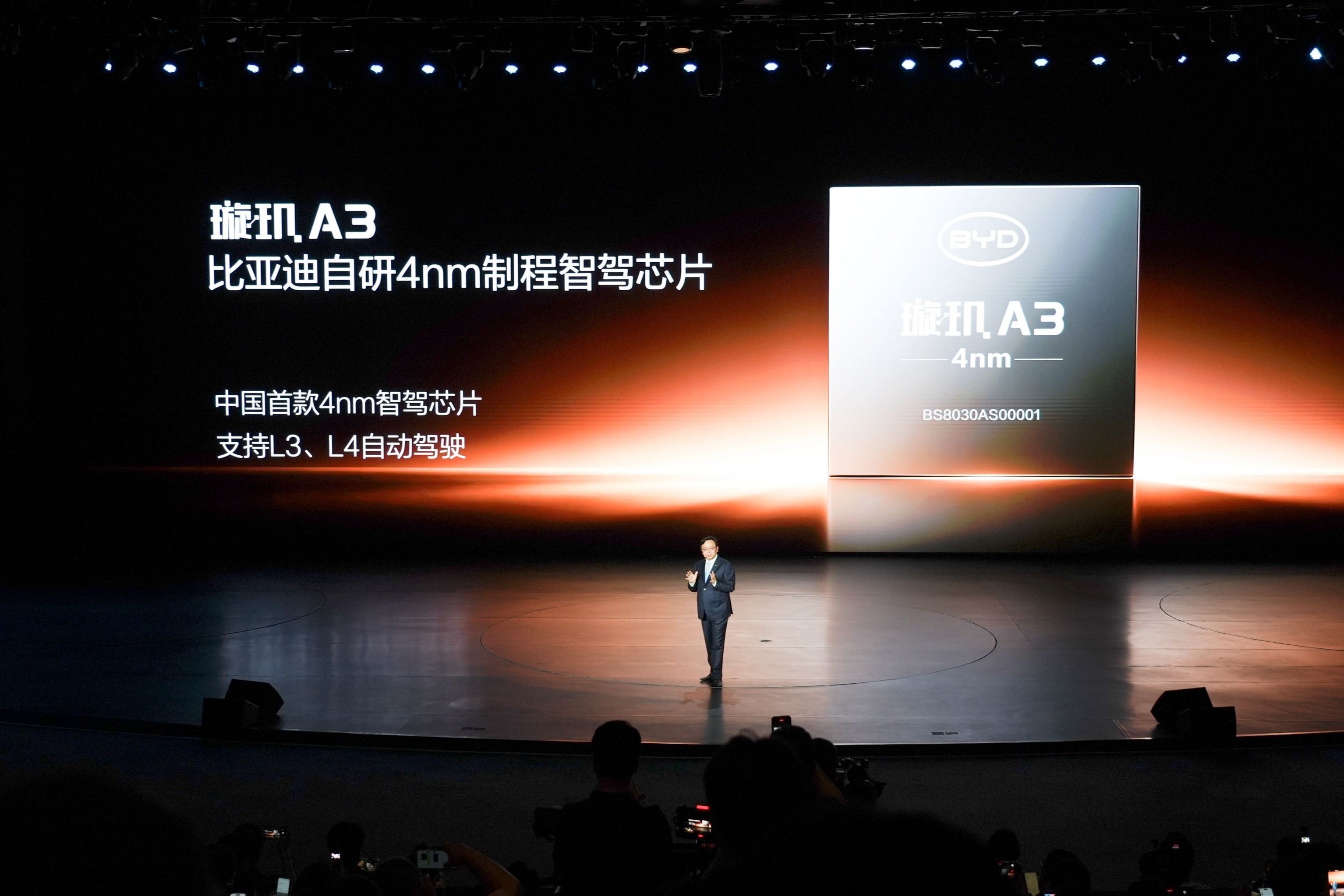 Homem de terno escuro em palco escuro com tela gigante exibindo o chip BYD Xuanji A3 de 4nm para direção autônoma L3 e L4