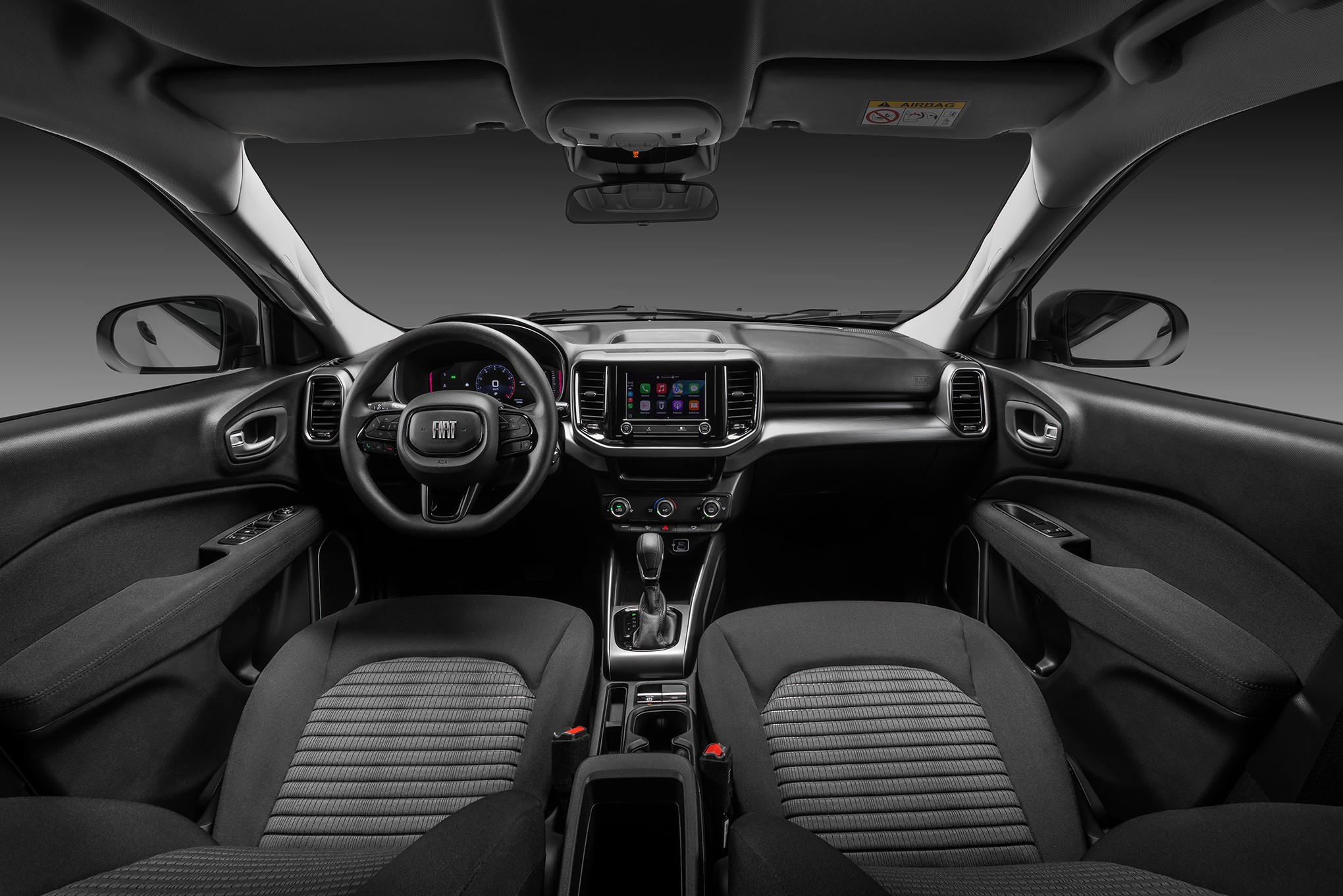 Interior de um carro moderno, com bancos dianteiros de tecido cinza e preto, painel escuro, volante com logo Fiat, tela multimídia central e câmbio automático