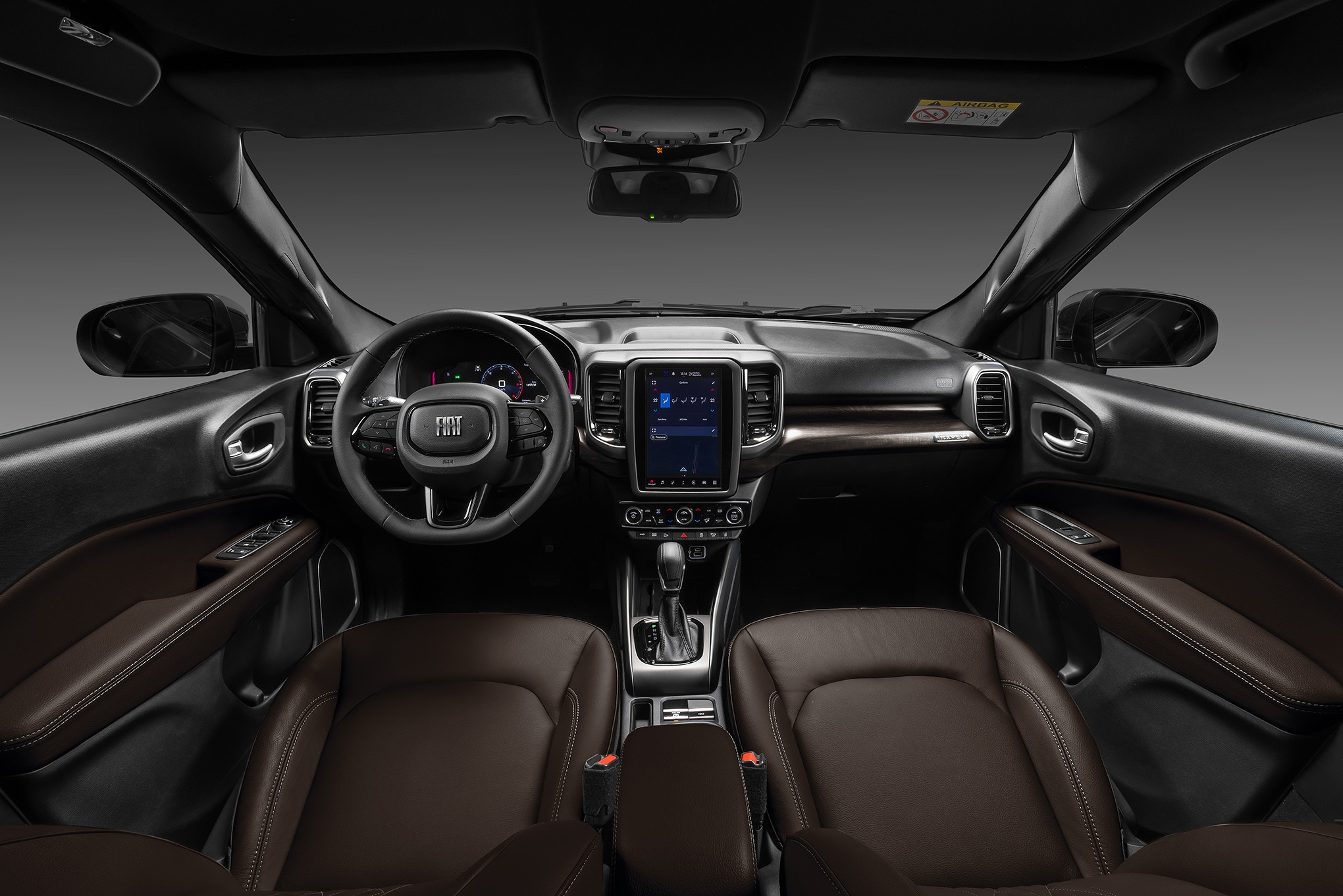 Interior de um carro moderno com bancos de couro marrom, painel escuro, volante multifuncional com logo Fiat e tela multimídia vertical no centro