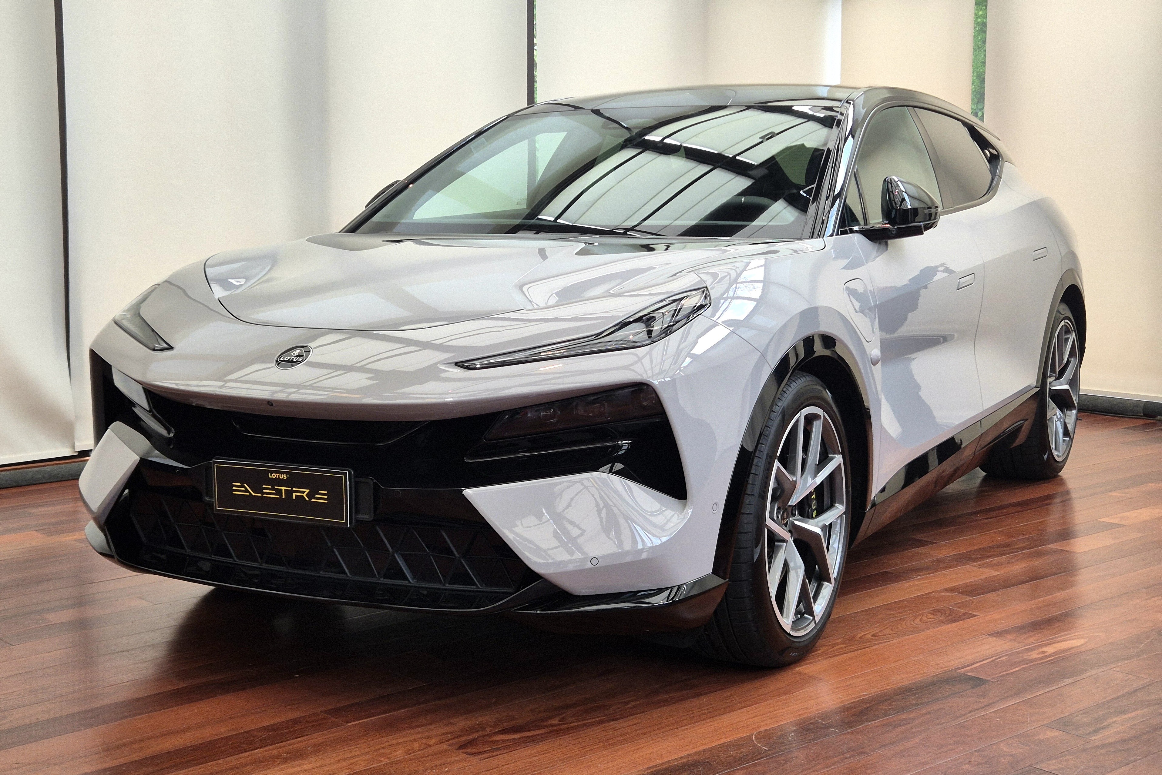 SUV elétrico Lotus Eletre cinza claro, com teto e detalhes pretos, estacionado em piso de madeira marrom brilhante