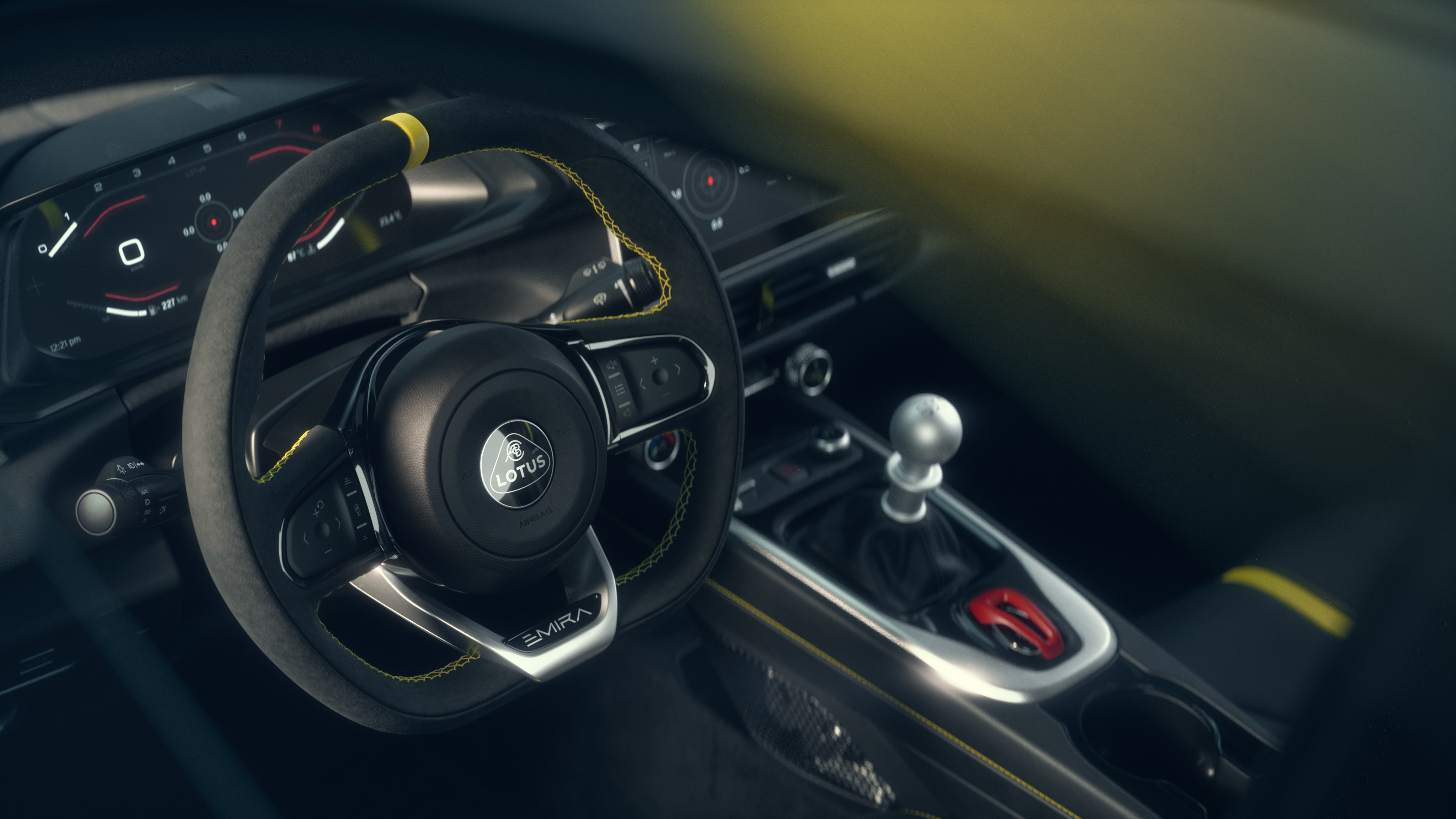 Interior de um carro esportivo Lotus Emira, mostrando o volante revestido em camurça com costura amarela, o painel digital e o câmbio manual com manopla prateada e detalhe vermelho no console central