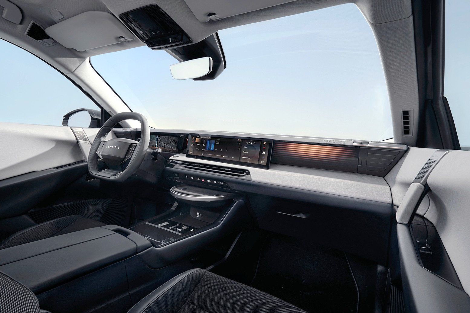 Interior moderno de um carro, com volante à esquerda, painel digital amplo e console central com porta-objetos e botões, em tons de cinza e preto, sob um céu azul claro visível pelo para-brisa