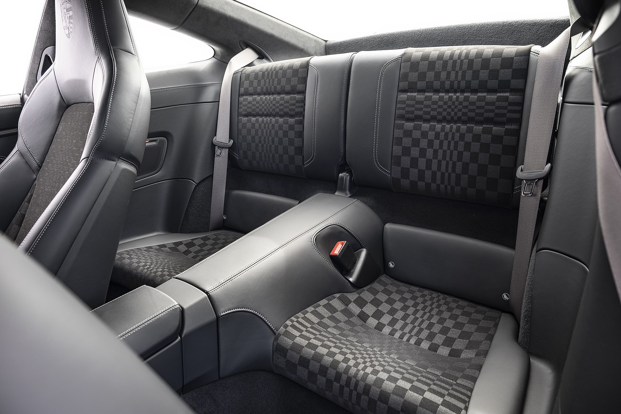 Interior de carro esportivo com bancos traseiros e parte do banco dianteiro em couro preto e tecido xadrez cinza escuro e preto, com cintos de segurança cinza