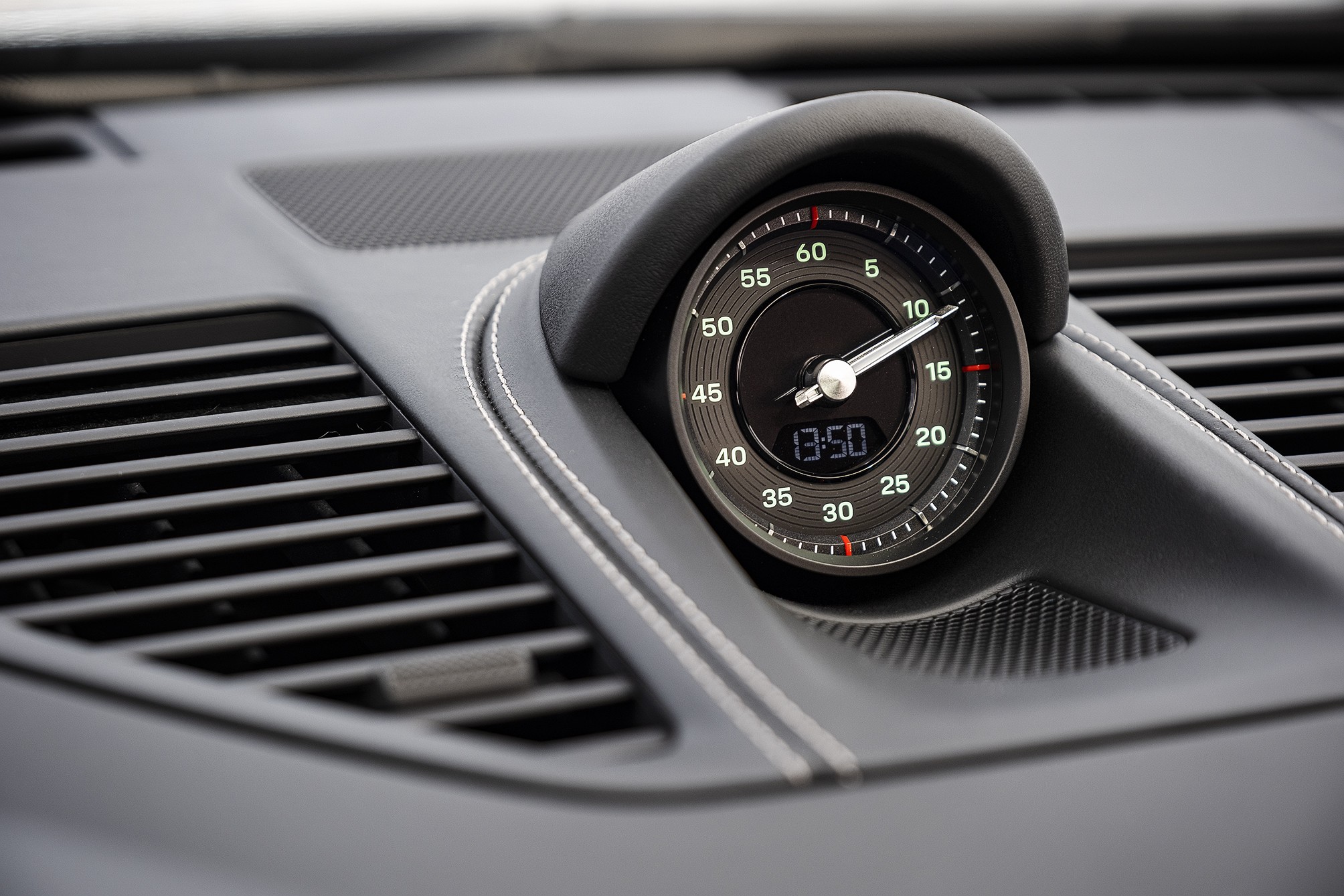 Cronômetro analógico e digital no painel de um carro, marcando 13:50, com costura branca e saída de ar ao lado