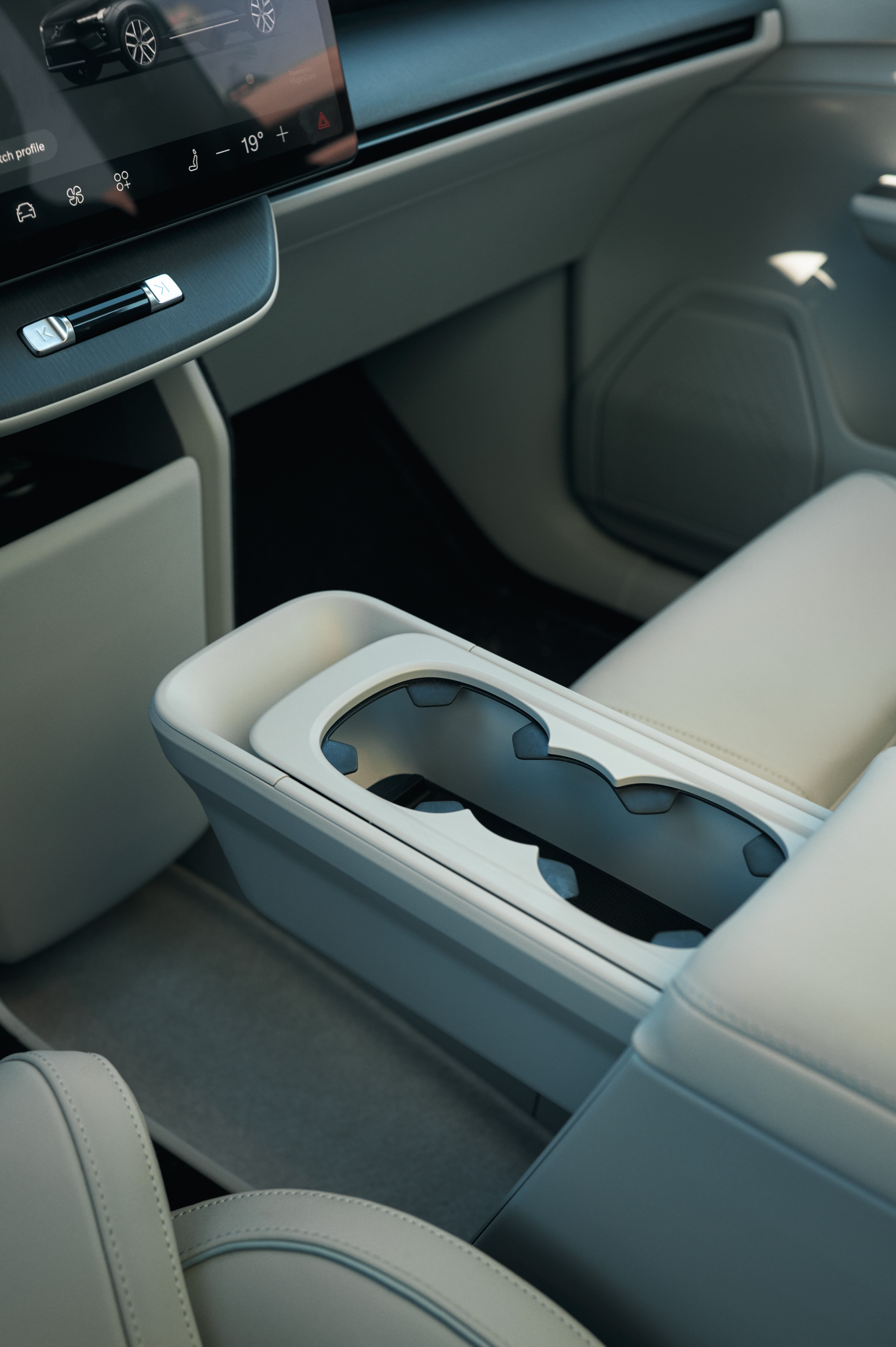 Interior de carro moderno com console central bege claro, porta-copos duplo e tela multimídia exibindo um carro e temperatura de 19 graus