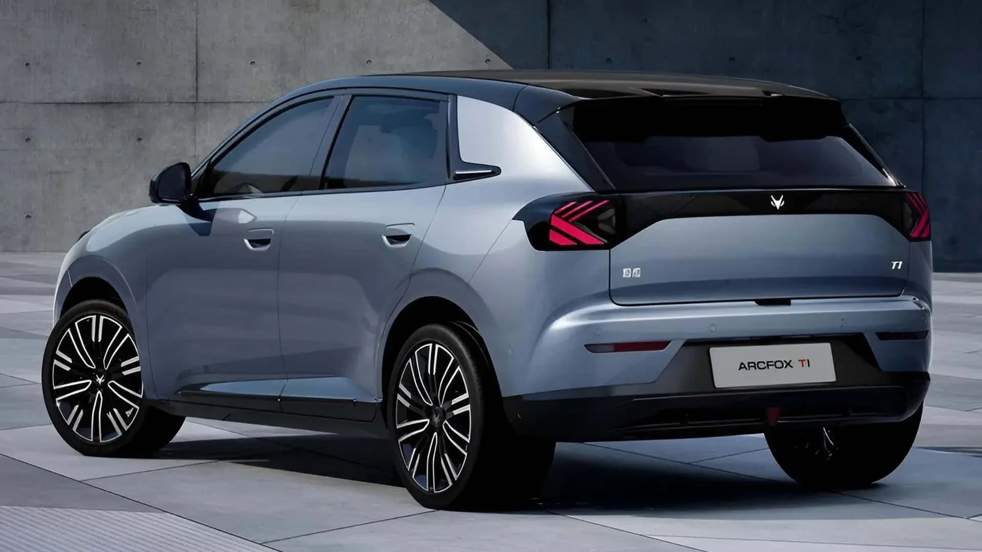 Carro ArcFox T1 cinza-azulado, com teto preto e rodas esportivas pretas e brancas, estacionado em piso de concreto claro com parede cinza ao fundo