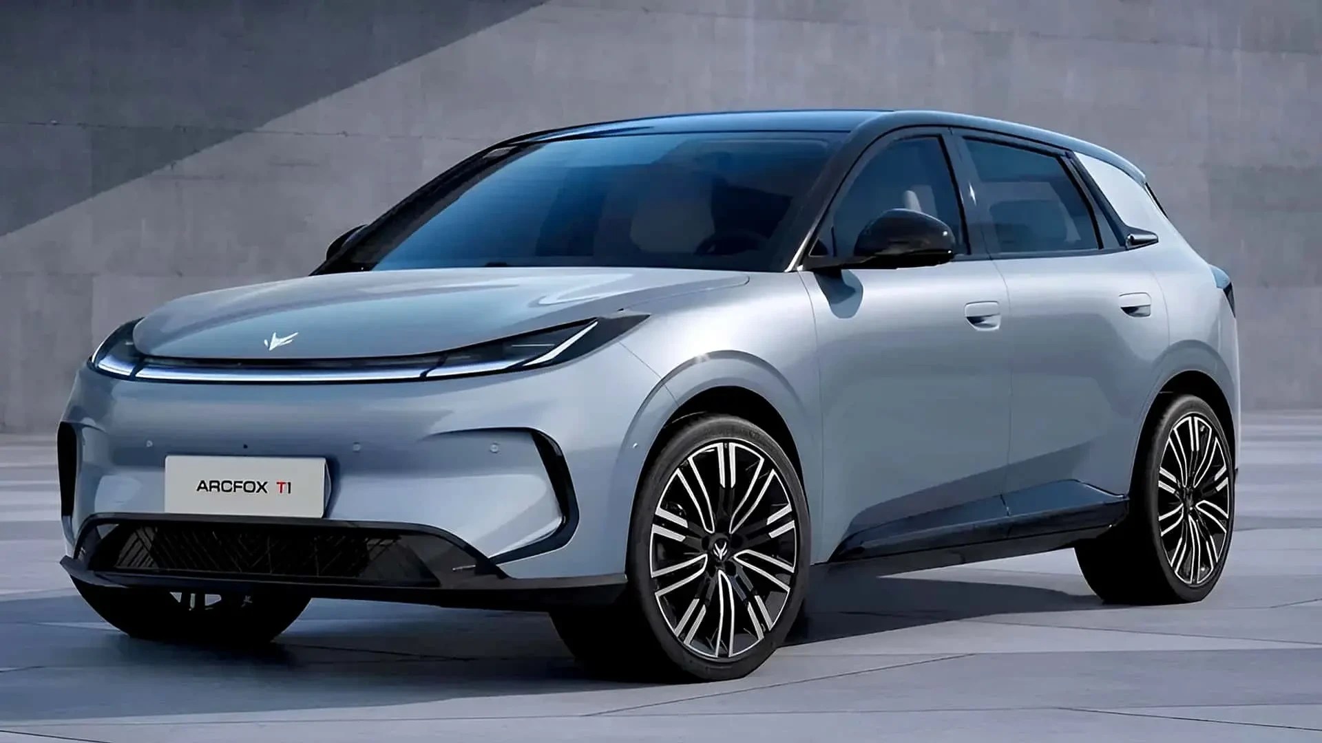 Carro ArcFox T1 cinza claro, com teto preto e rodas pretas com detalhes prateados, estacionado em um piso cinza claro com uma parede cinza escuro ao fundo