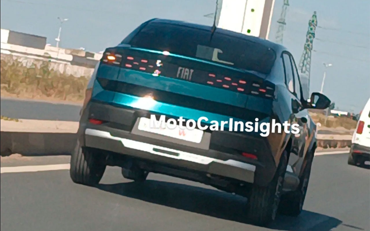 Traseira de um carro Fiat azul-petróleo, com lanternas horizontais de LED e para-choque preto com detalhe prateado, em uma estrada sob luz solar