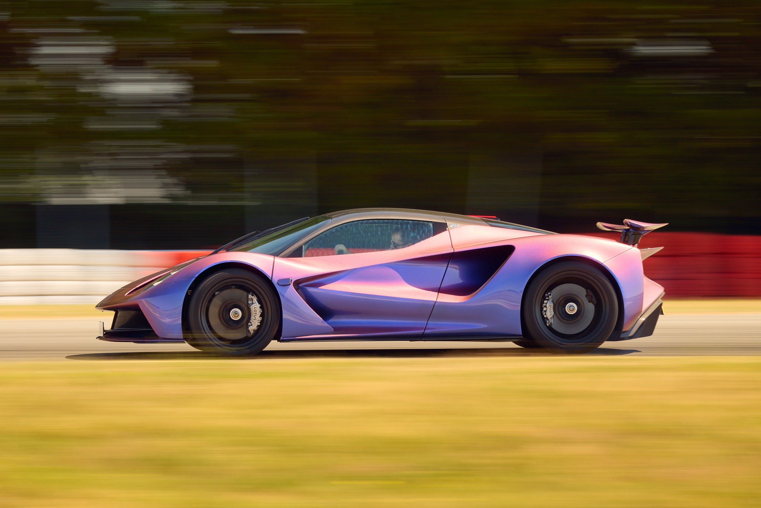Carro esportivo roxo e rosa metálico em alta velocidade numa pista de corrida, com o fundo borrado por movimento