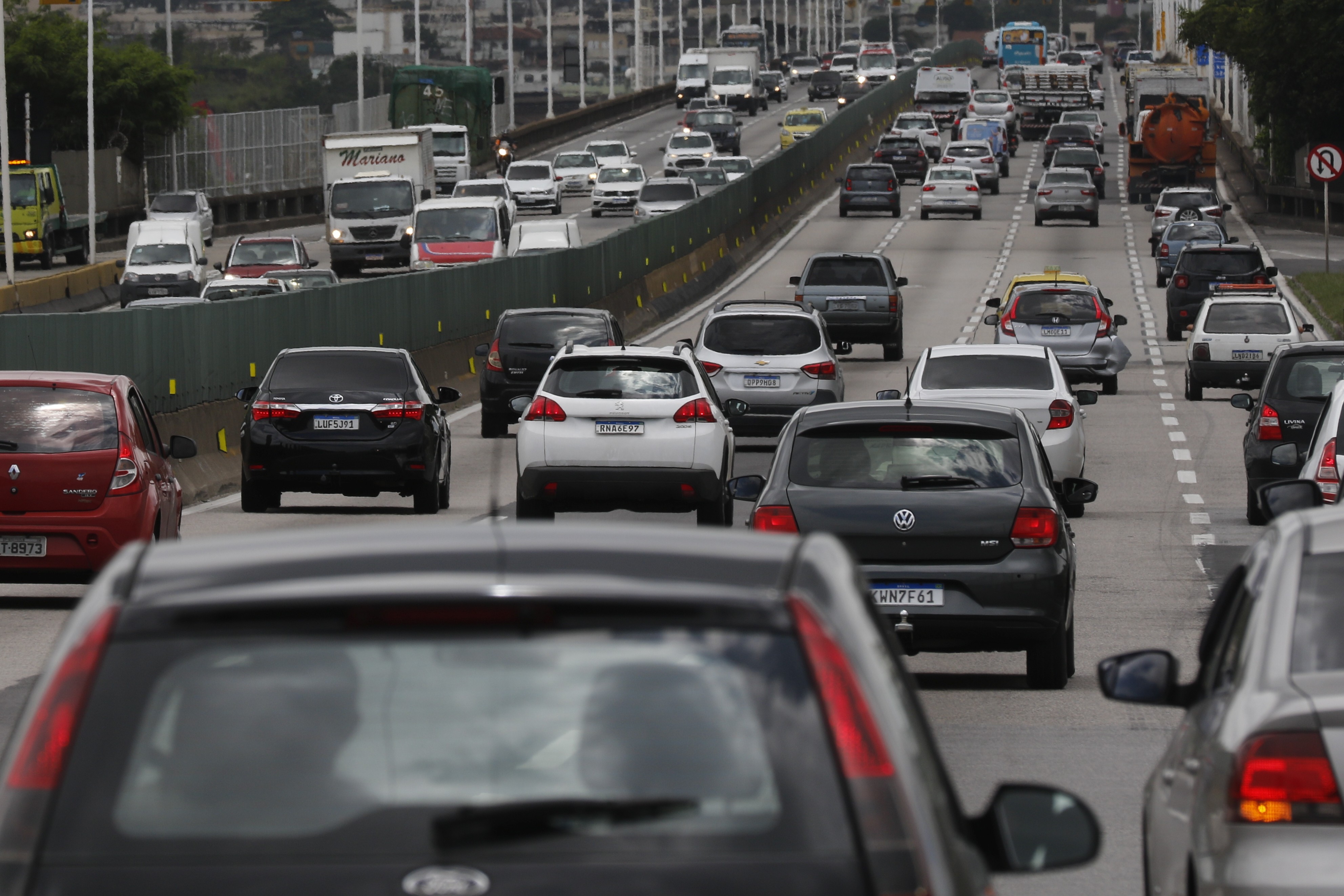 Tráfego intenso de veículos em uma rodovia com várias pistas, carros e caminhões em movimento lento, sob um céu nublado
