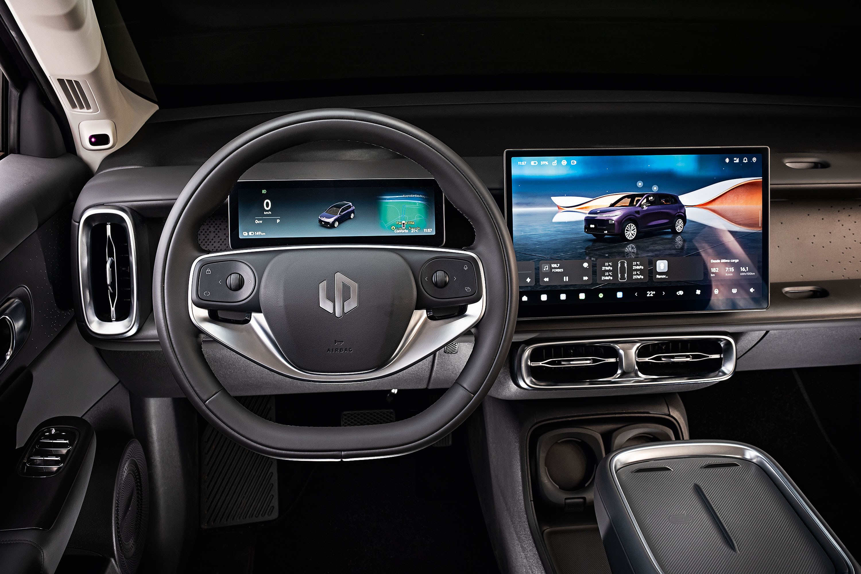 Interior de um carro moderno com volante preto e cinza, painel digital exibindo um carro roxo e tela multimídia grande com o mesmo veículo. Detalhes de saídas de ar cromadas e console central com porta-copos.