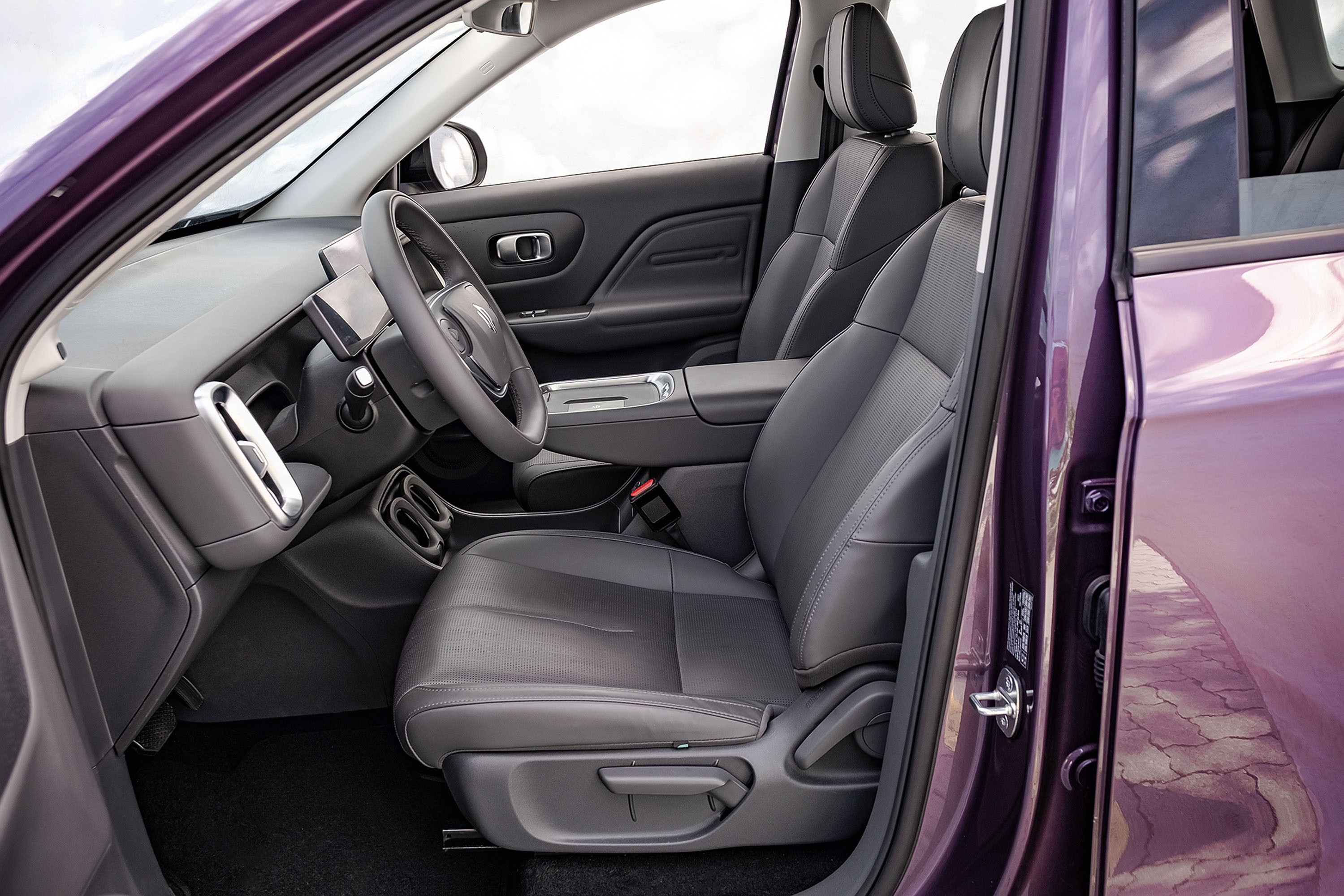 Interior de um carro roxo com a porta do motorista aberta, mostrando o banco de couro cinza escuro, volante e painel com detalhes prateados