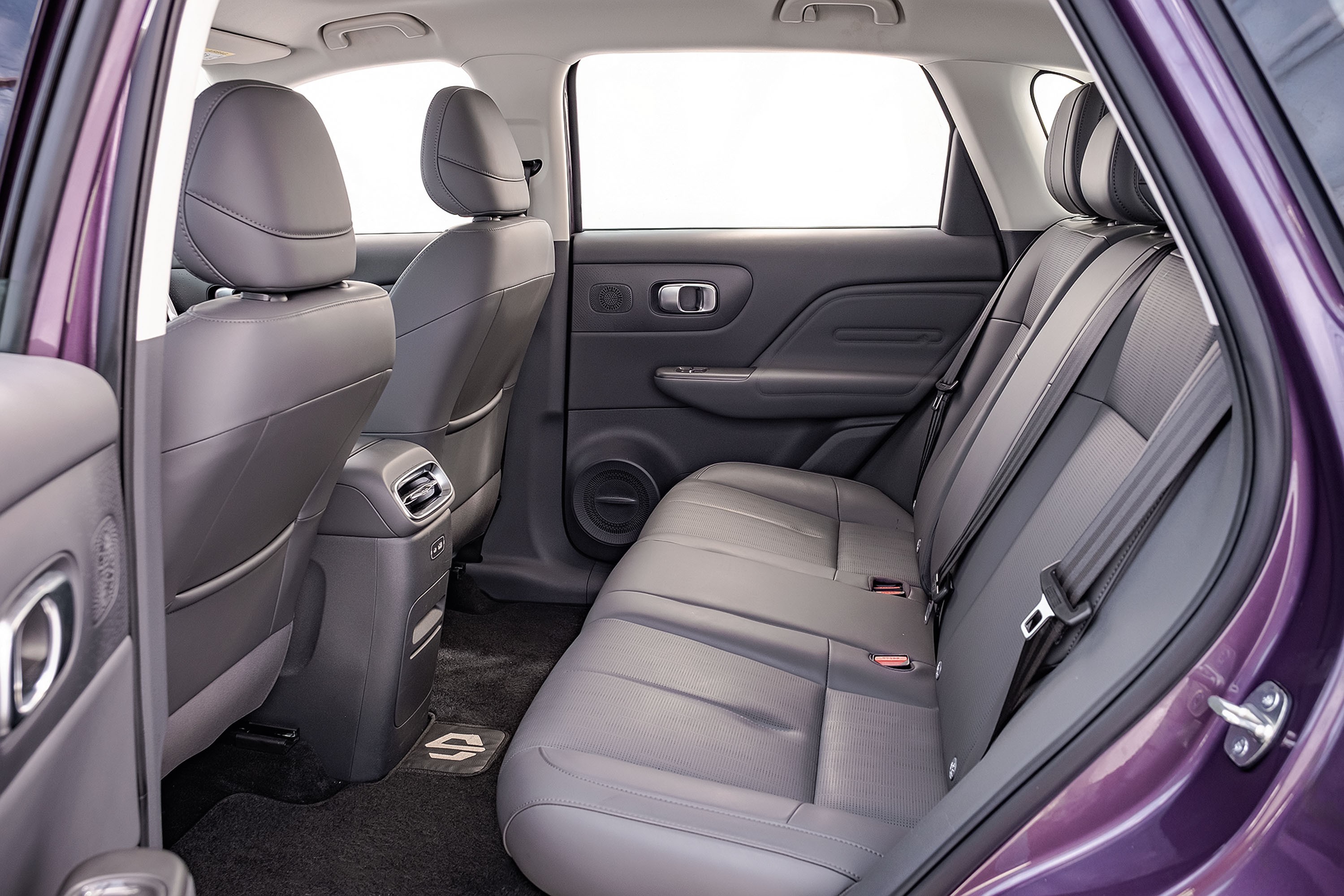 Interior de um carro roxo com bancos traseiros de couro cinza escuro, cinto de segurança visível, e console central com saídas de ar