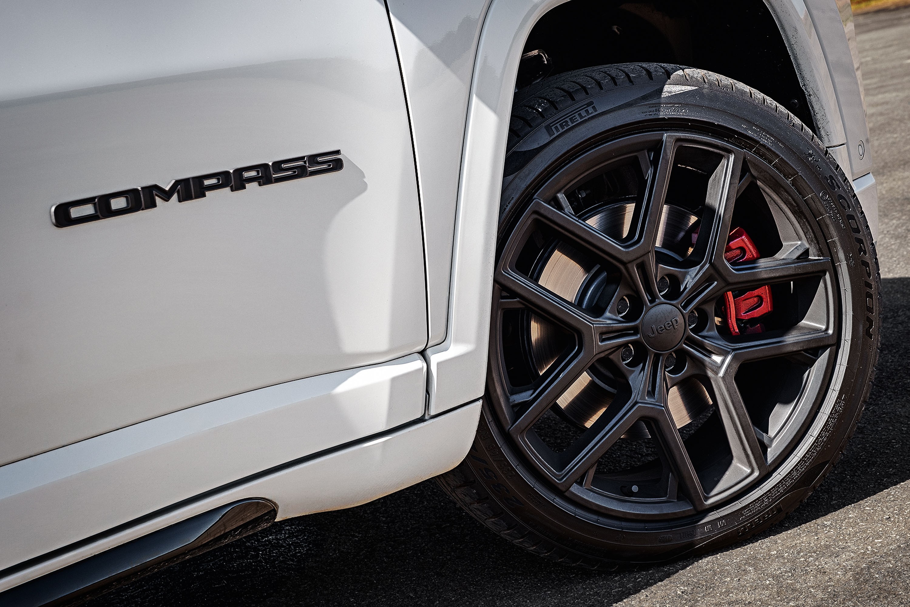 Lateral de um carro branco com o emblema COMPASS em preto, próximo a uma roda preta com detalhes em vermelho nos freios