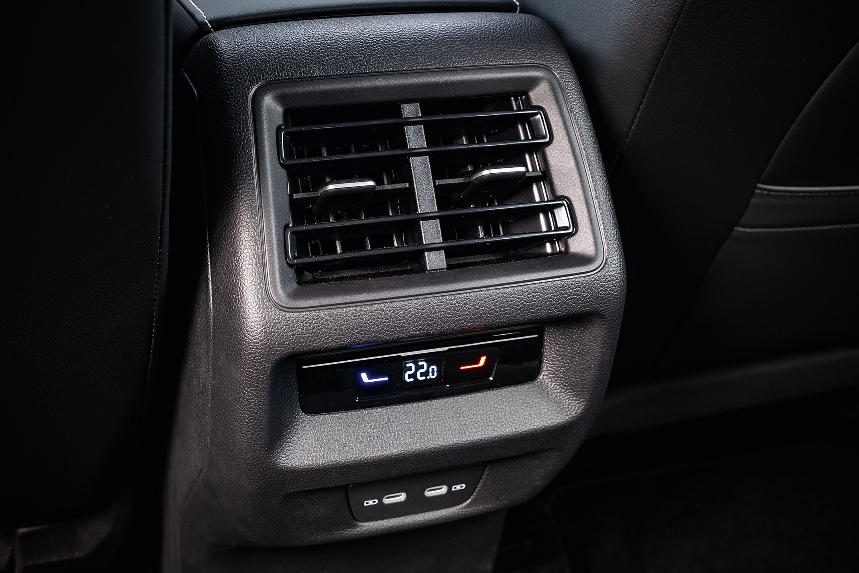 Saída de ar condicionado traseira de um carro, com display digital mostrando 22.0 graus Celsius, botões de temperatura em azul e vermelho, e duas portas USB-C abaixo