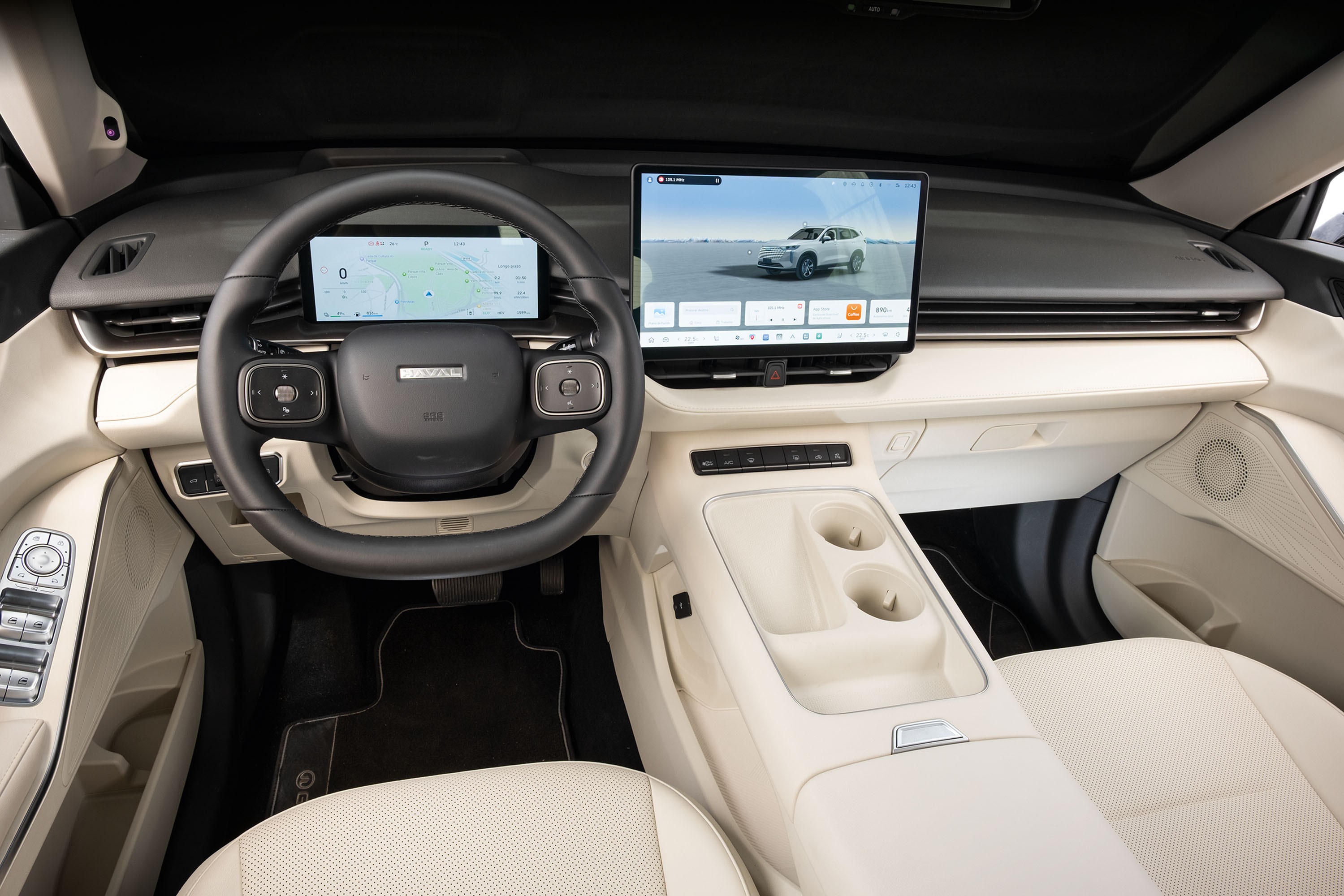 Interior de carro moderno com volante preto e dois monitores digitais. O monitor esquerdo exibe um mapa de navegação, e o direito mostra um SUV branco em uma paisagem desértica. O painel e os bancos são em tons claros de bege, com detalhes em preto e prata. O console central possui porta-copos.
