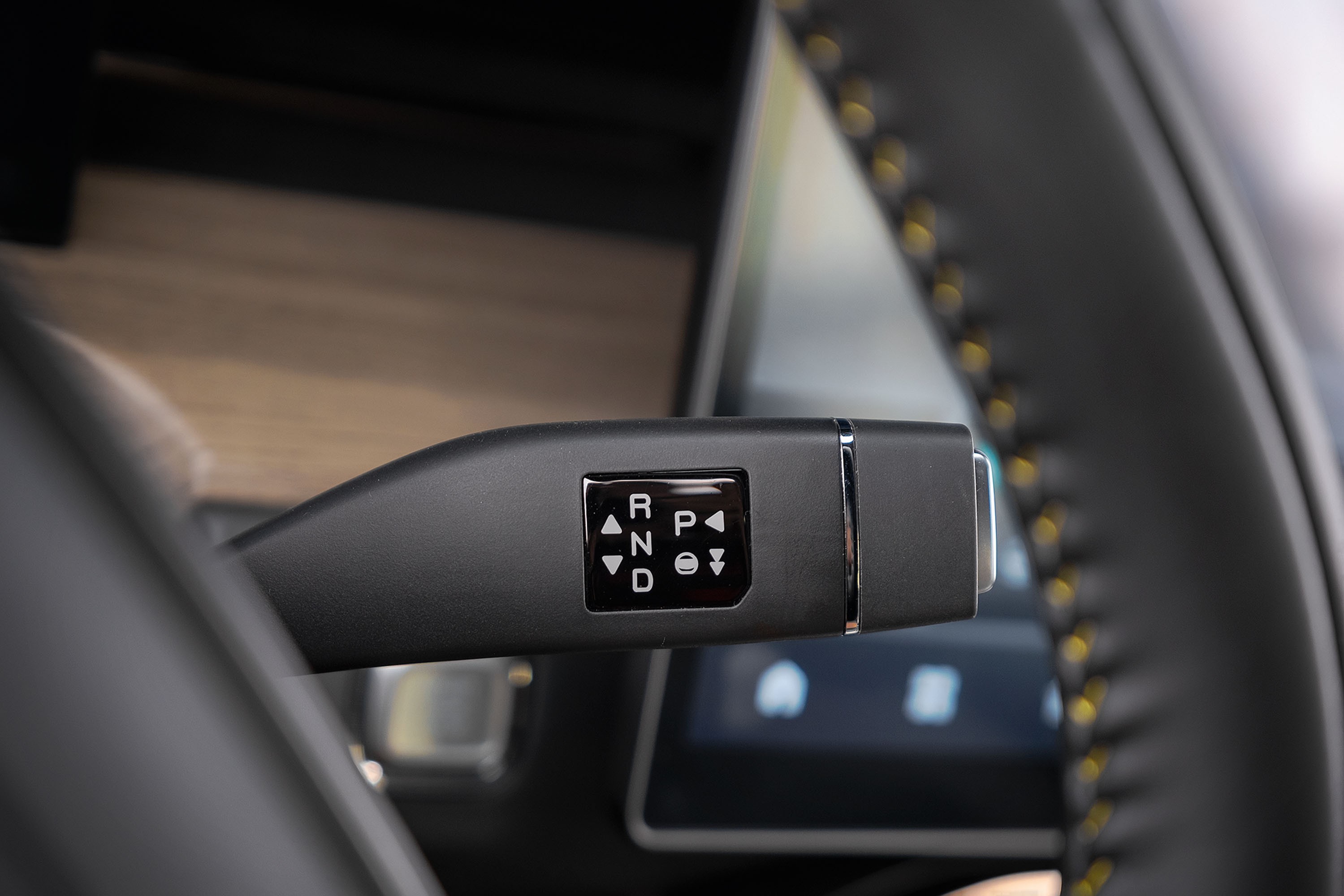 Alavanca de câmbio automática preta com botões para R, N, D e P, além de setas para cima e para baixo, no interior de um carro moderno com volante de couro e costura amarela