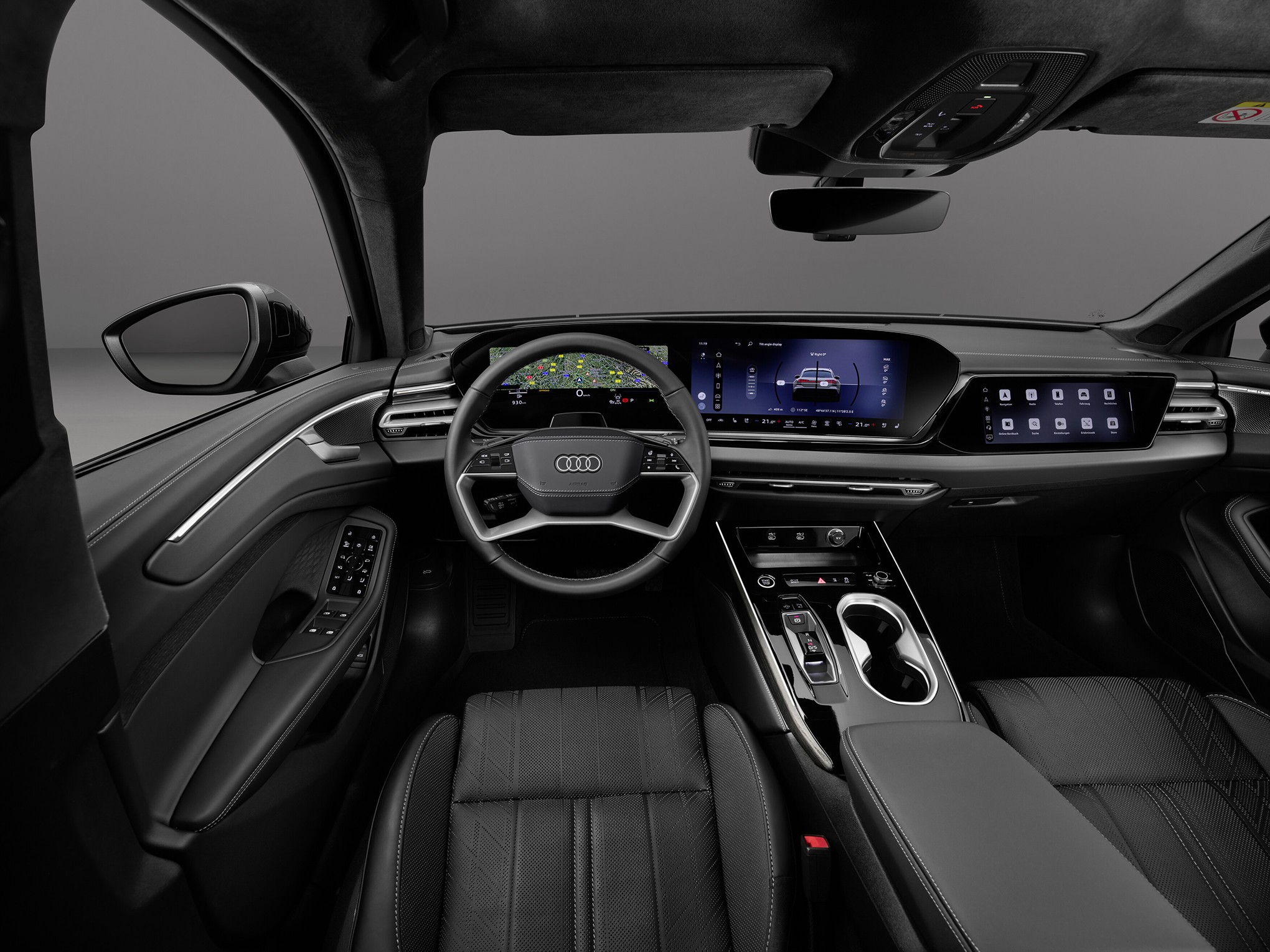 Interior de um carro Audi moderno, com volante multifuncional, painel digital exibindo mapa e informações do veículo, e console central com porta-copos e controles táteis. Os bancos são de couro preto, e o acabamento interno é escuro com detalhes cromados. A visão é do lado do motorista, mostrando o espelho retrovisor lateral esquerdo
