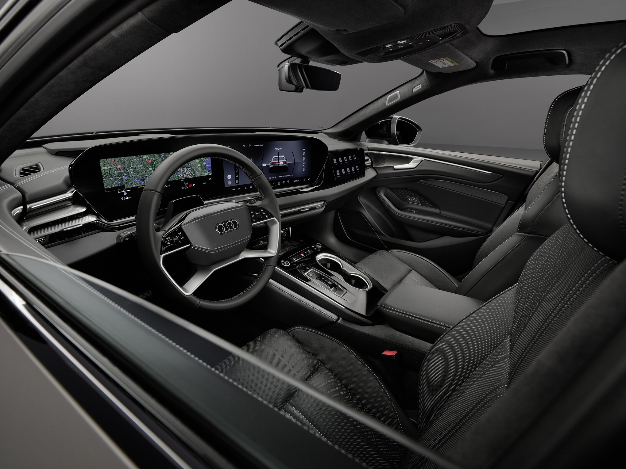 Interior de um carro Audi moderno, com volante multifuncional e painel digital exibindo um mapa. Bancos de couro pretos com costura branca, console central com porta-copos e câmbio automático. O ambiente é sofisticado e tecnológico