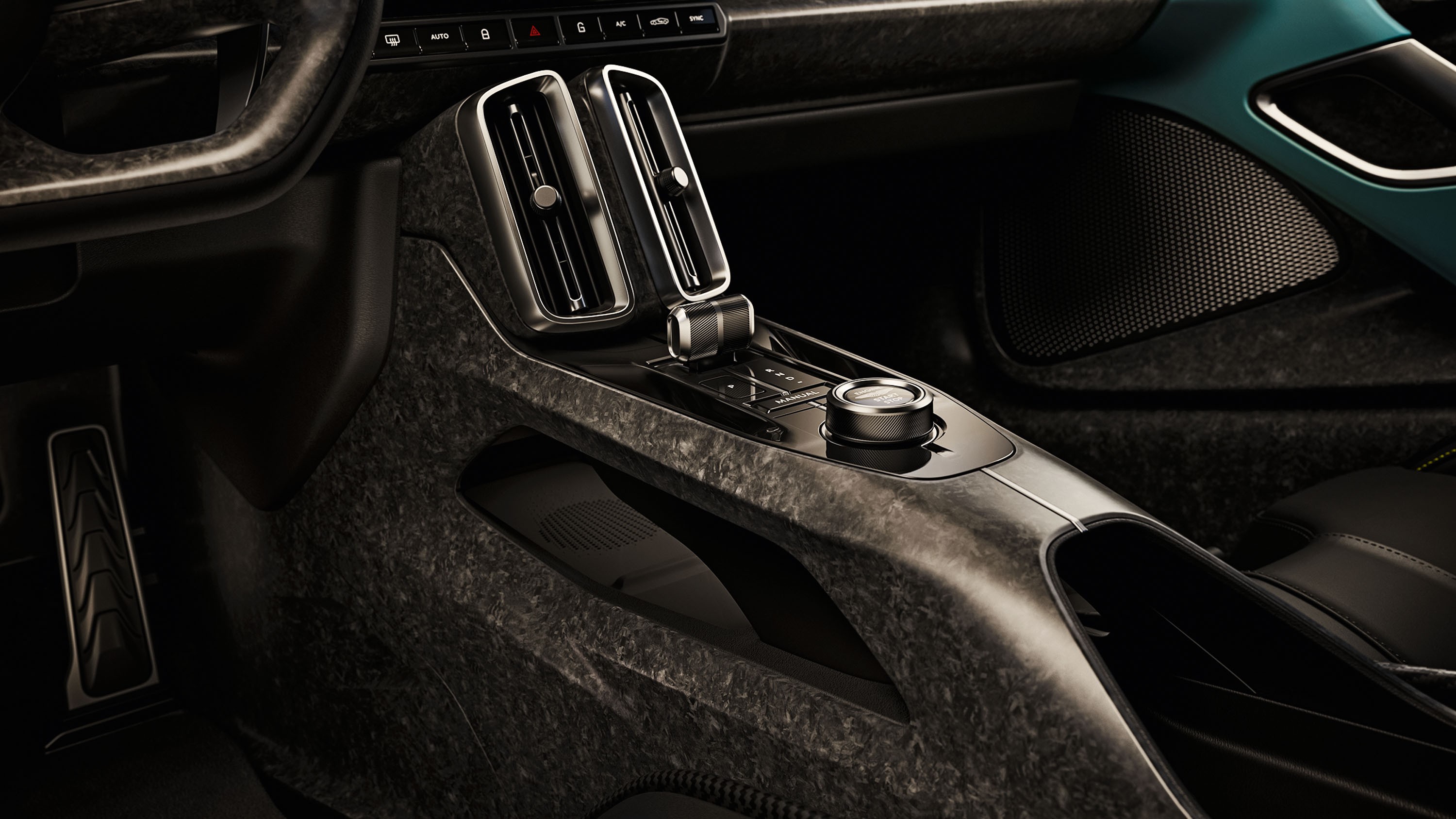 Interior de carro moderno com console central em tom escuro texturizado, dois difusores de ar verticais, alavanca de câmbio e um botão giratório prateado. O volante e o pedal esquerdo são visíveis, com detalhes em azul-petróleo na porta direita