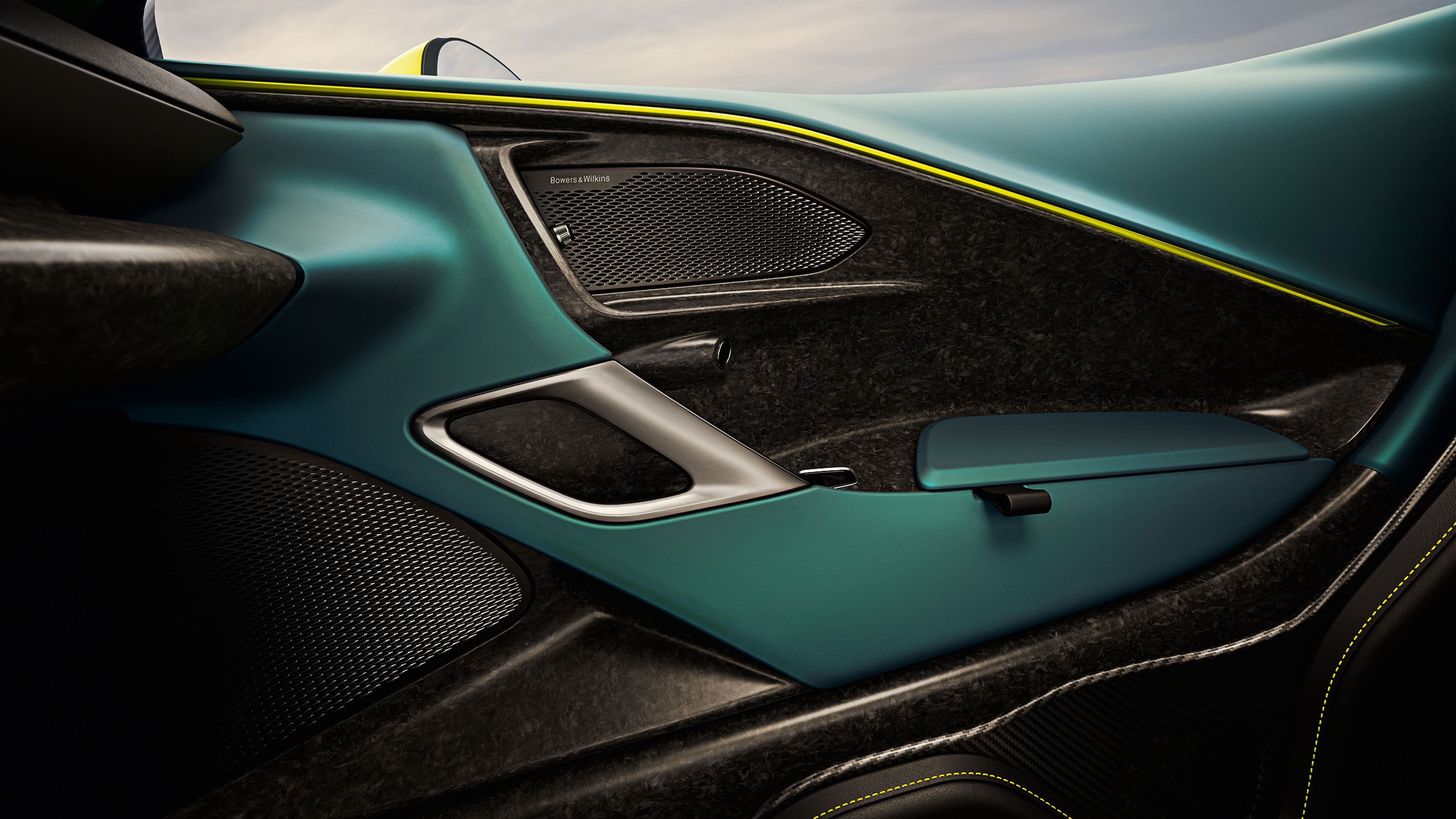 Interior de carro esportivo com porta em tons de azul-petróleo e preto, detalhes em fibra de carbono e costura amarela. Há uma alça de porta prateada e dois alto-falantes com grade metálica. O design é moderno e luxuoso