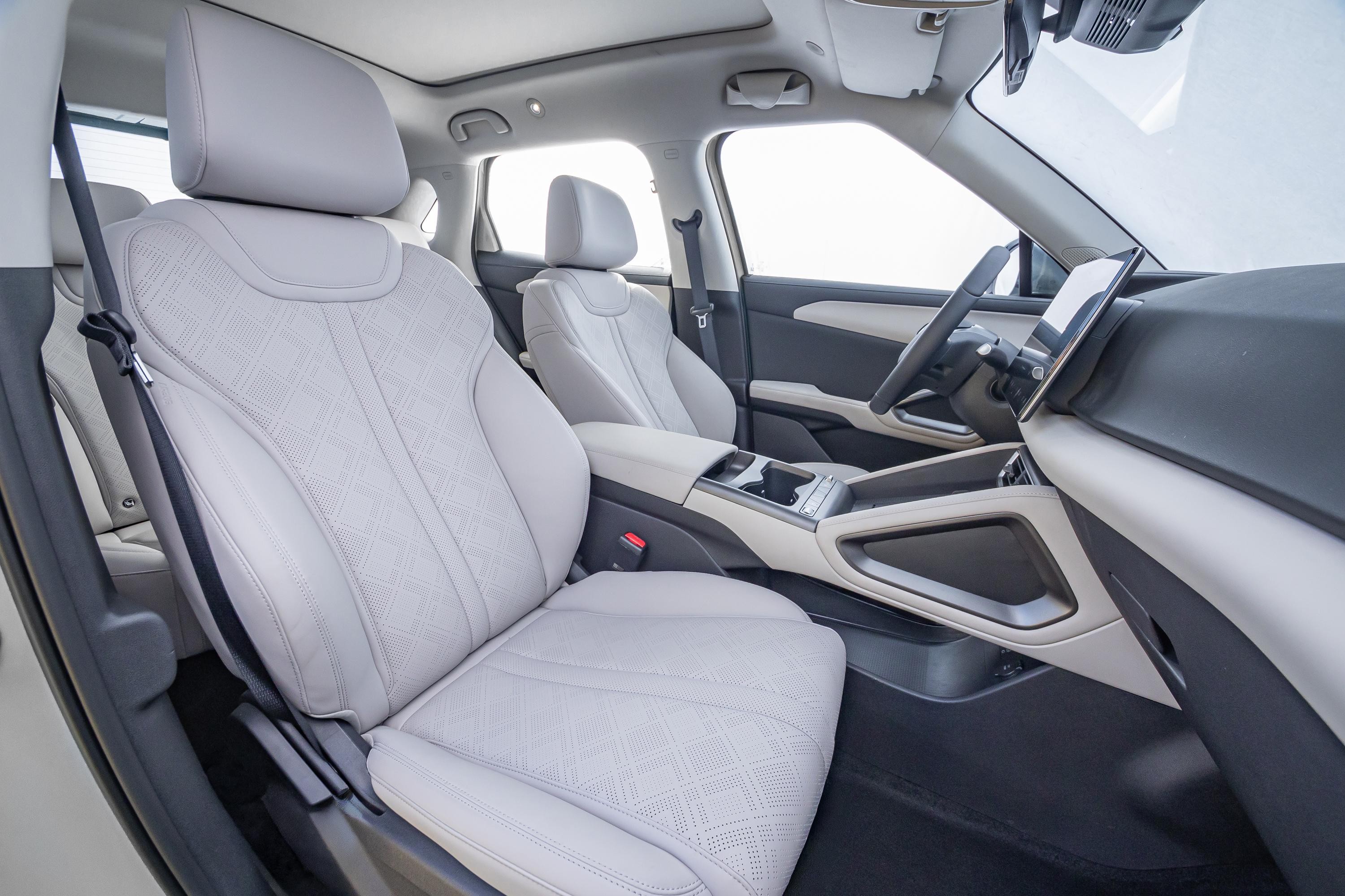 Interior de um carro moderno com bancos de couro cinza claro, detalhes em branco e preto no painel e portas, e uma tela digital no console central