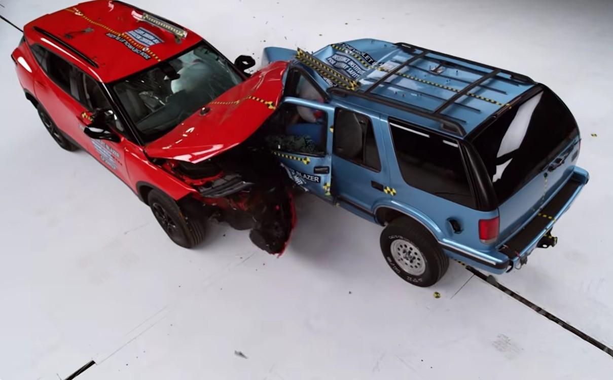 Dois carros de teste, um SUV vermelho e um SUV azul, colidiram frontalmente, com o vermelho amassado na frente e o azul na lateral do motorista, ambos com sensores amarelos e pretos espalhados pela carroceria