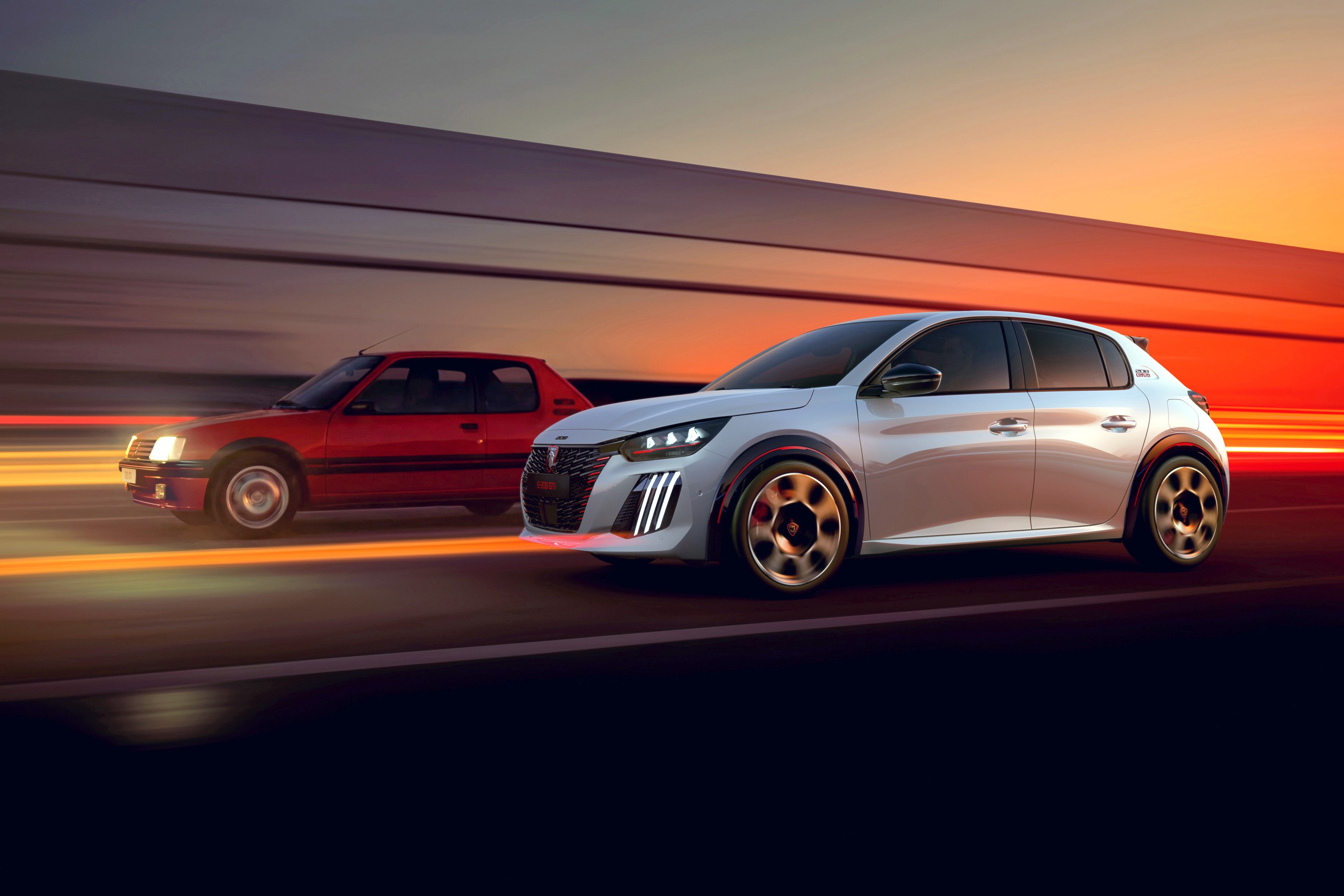 Dois carros Peugeot em movimento, um modelo antigo vermelho à esquerda e um moderno branco à direita, com luzes de LED acesas, em uma estrada com o céu alaranjado do pôr do sol ao fundo