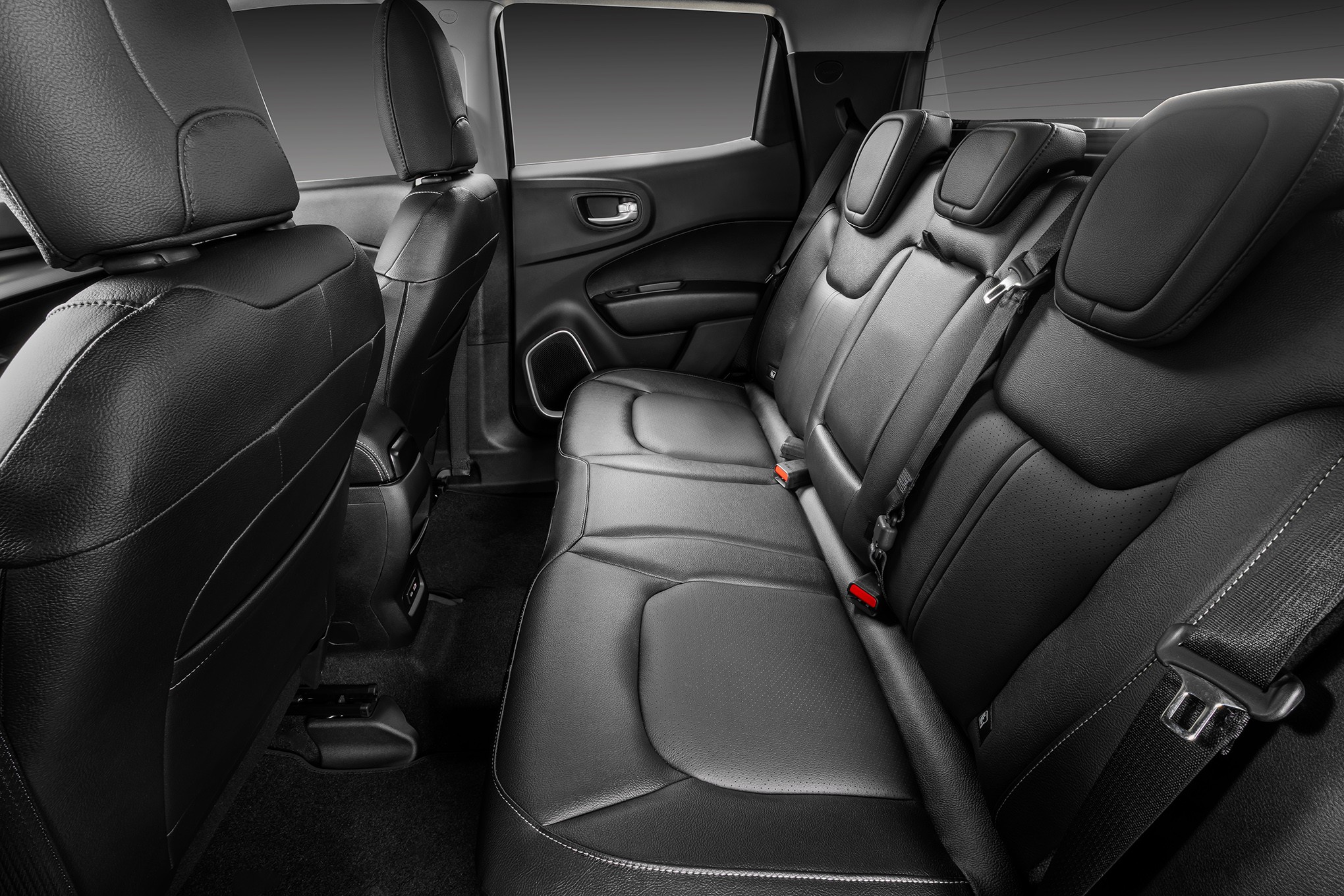 Interior de carro com bancos traseiros de couro preto, cintos de segurança visíveis e encostos de cabeça ajustáveis, destacando o conforto e espaço