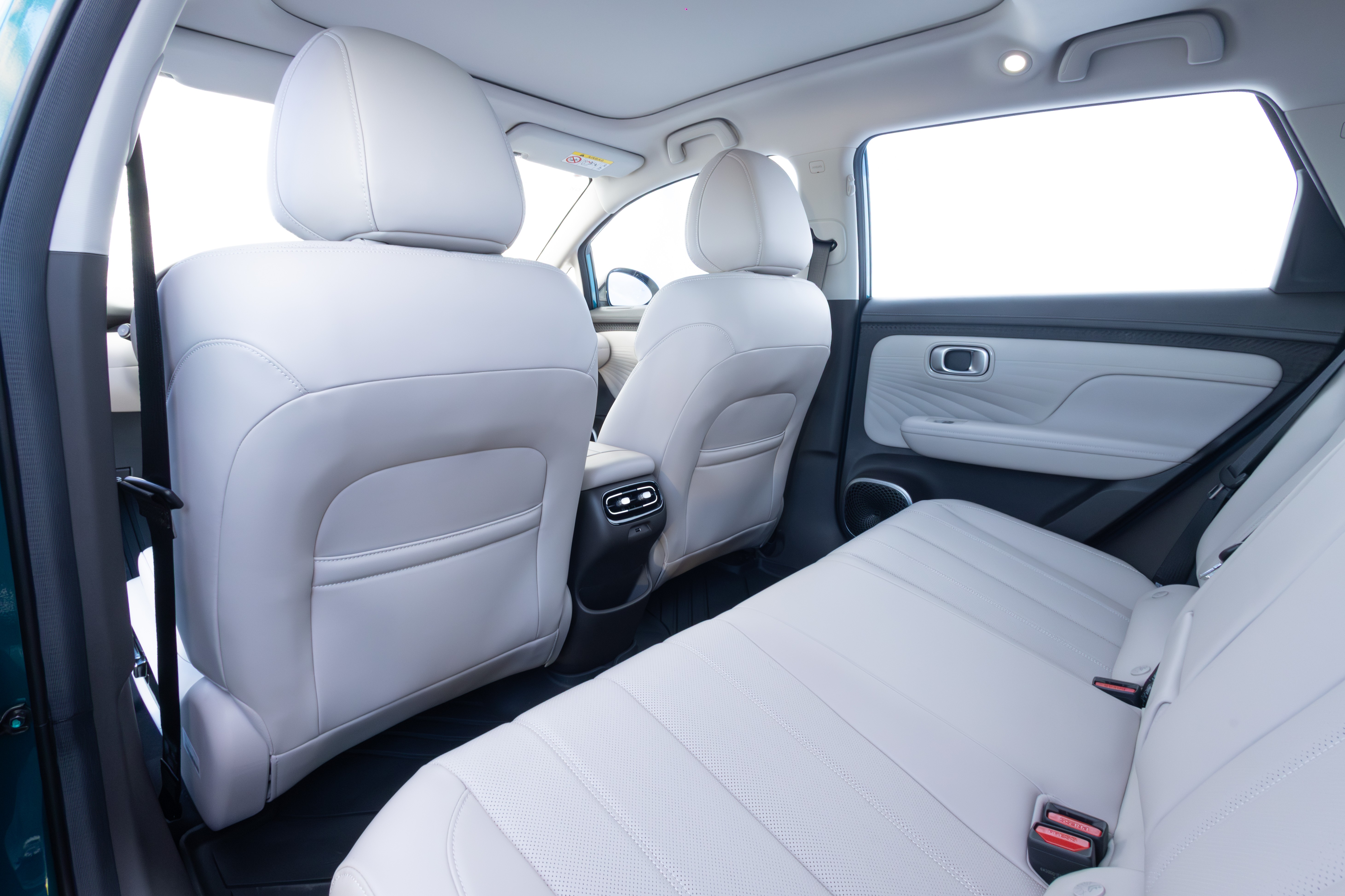 Interior de carro com bancos de couro branco, vista do banco traseiro para os assentos dianteiros e porta lateral, com janelas claras