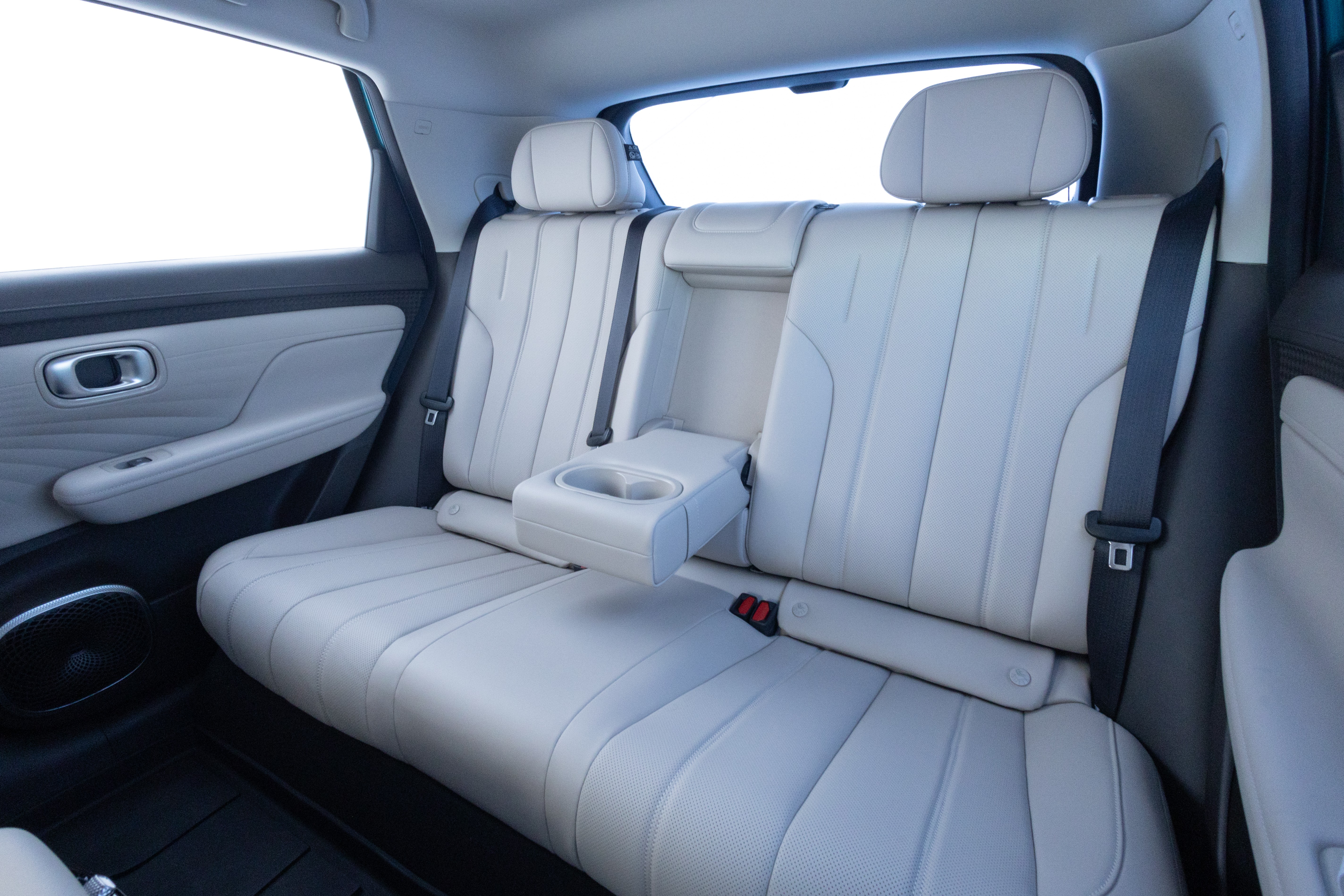 Interior de um carro com bancos traseiros de couro bege claro, cinto de segurança preto e apoio de braço central rebatível com porta-copos
