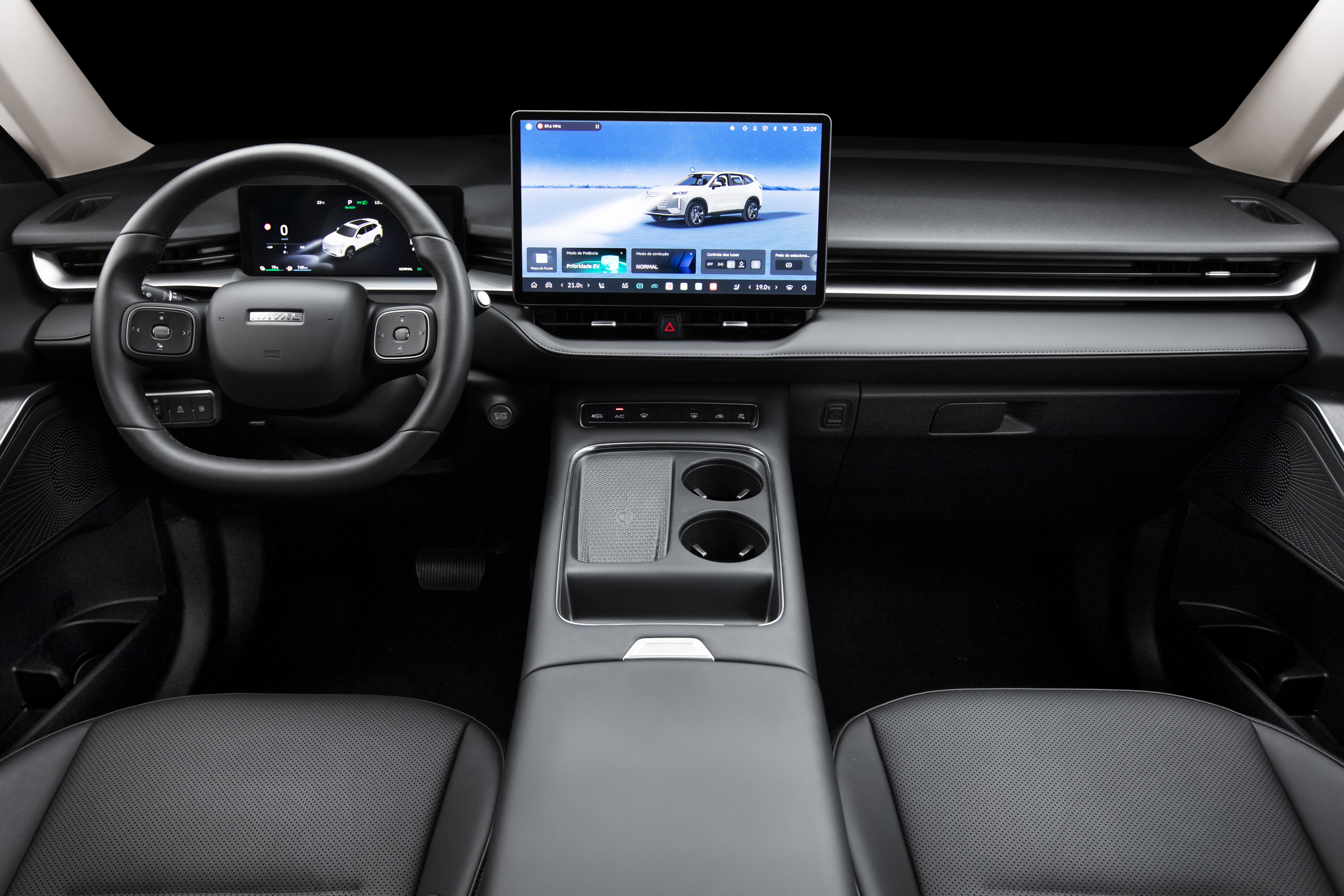 Interior de um carro moderno com painel escuro, volante multifuncional e duas telas digitais. A tela central exibe um SUV branco em uma paisagem nevada, enquanto a tela menor atrás do volante mostra um mapa com o mesmo veículo. Há um console central com porta-copos e apoio de braço, e bancos de couro pretos visíveis