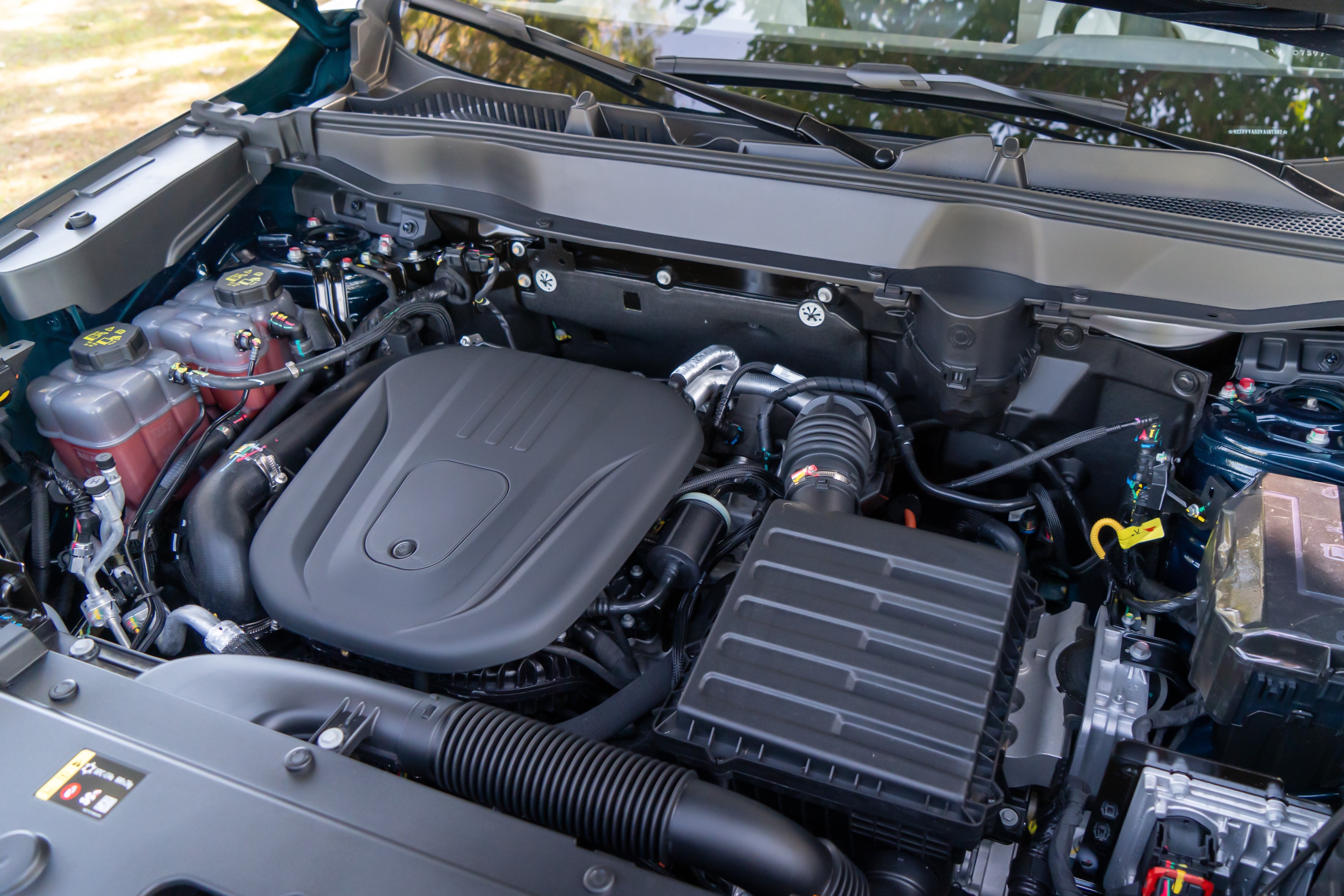Compartimento do motor de um carro, com o motor coberto por uma capa preta, filtros de ar e reservatórios de fluidos visíveis
