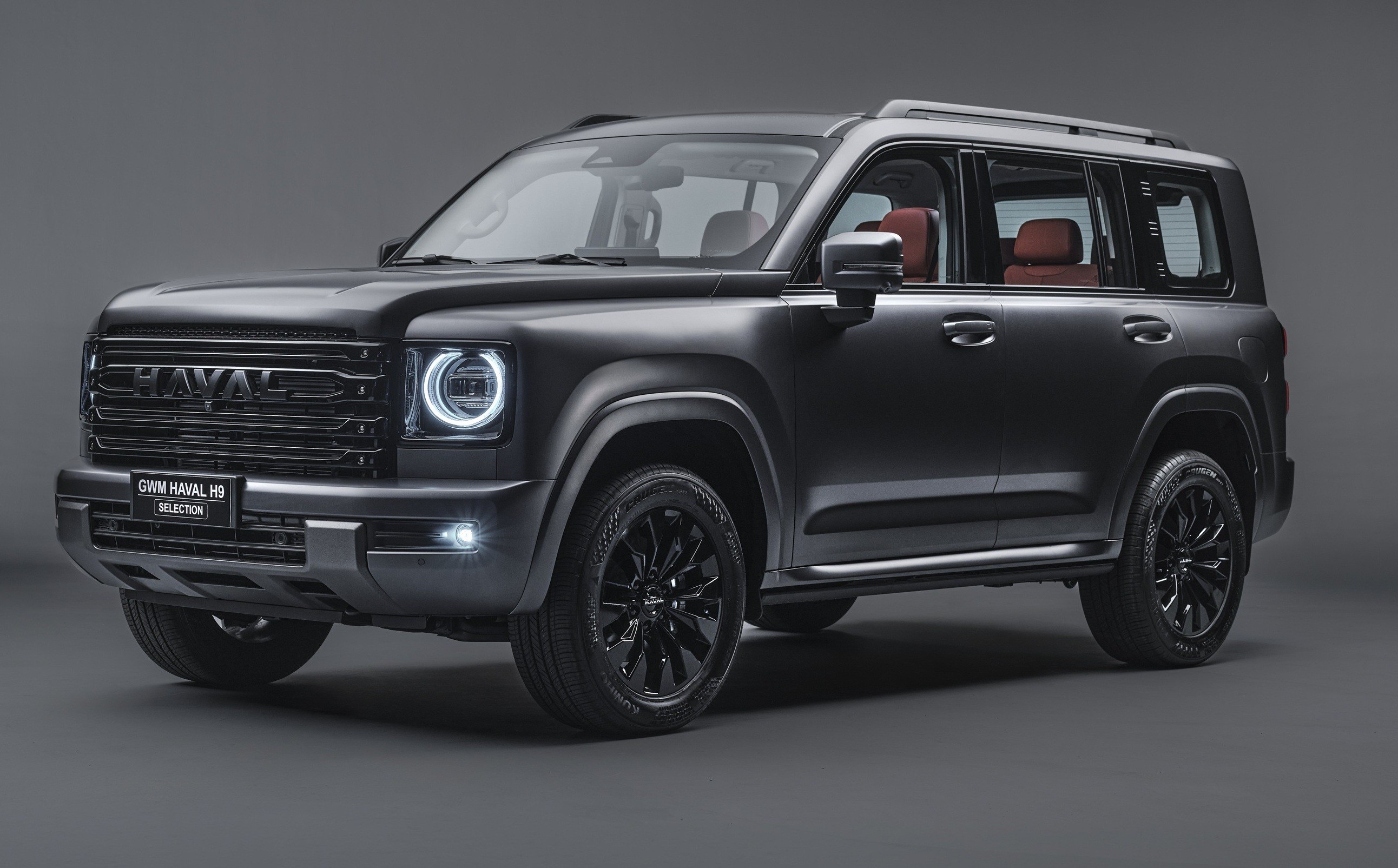 SUV Haval H9 preto fosco, com faróis redondos acesos, grade frontal escura e rodas pretas, exibindo interior com bancos marrons