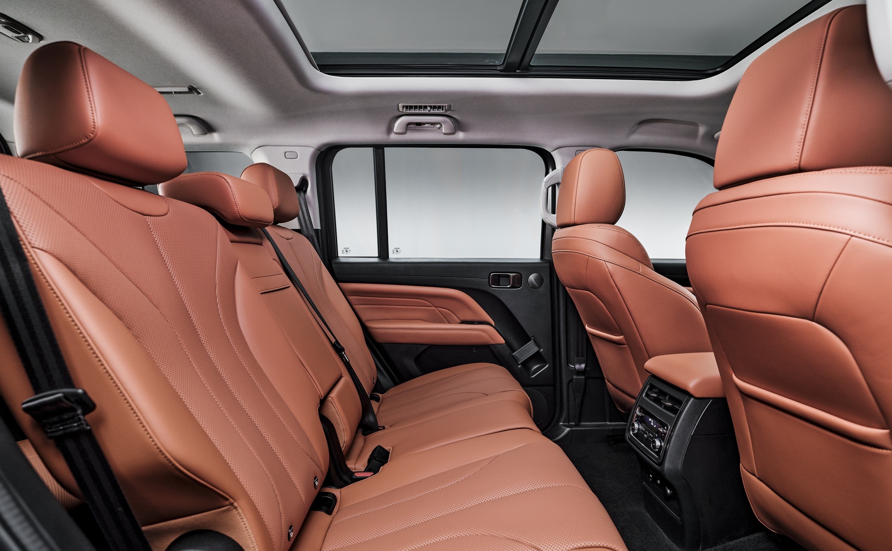 Interior de um carro com bancos de couro marrom-claro, incluindo a segunda e terceira fileiras. O teto solar panorâmico está visível, e há um painel de controle de ar-condicionado na parte traseira do console central