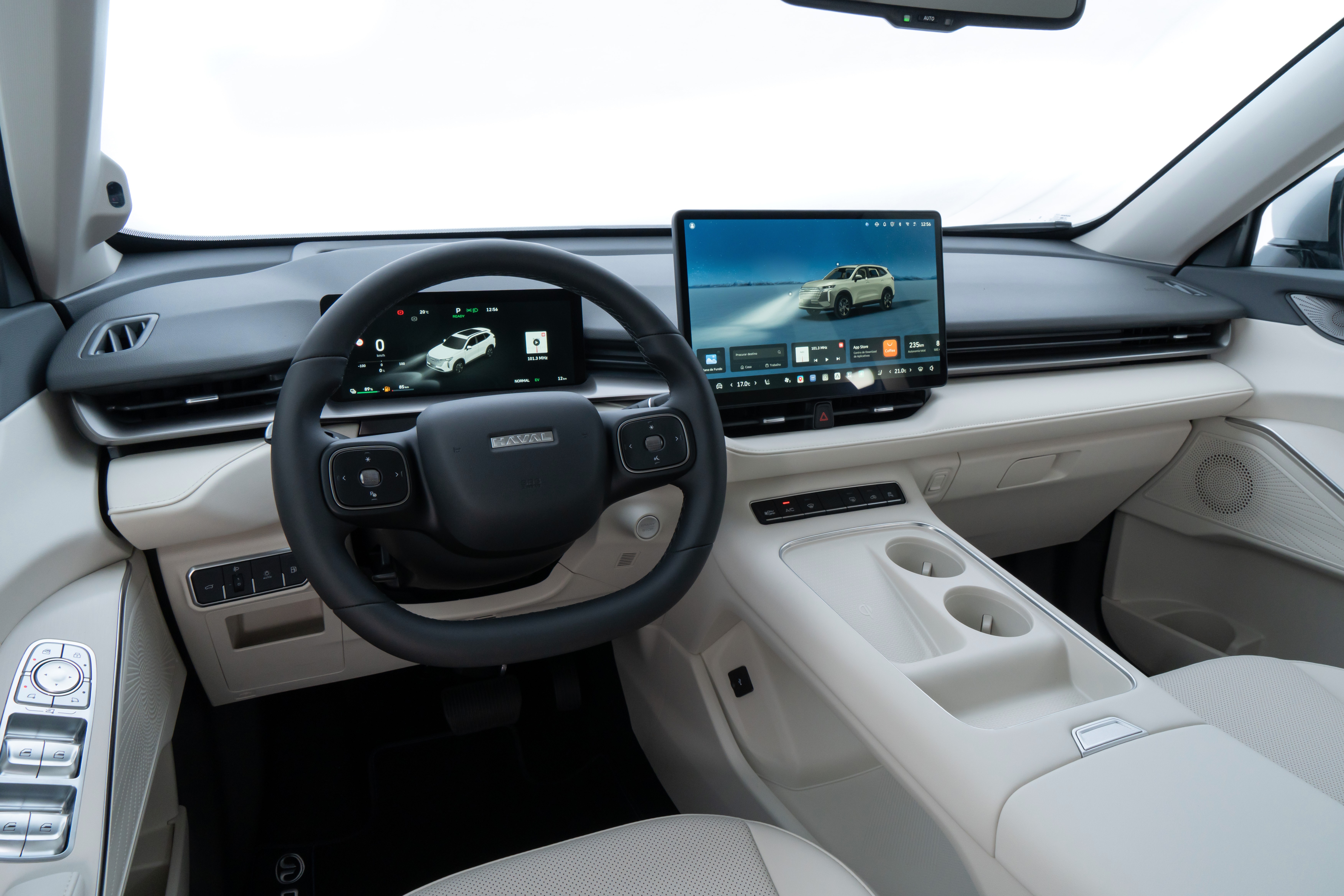 Interior moderno de um carro, com volante preto e painel claro. Dois monitores digitais exibem um SUV branco em diferentes cenários, um com faróis acesos. O console central tem porta-copos e botões de controle.