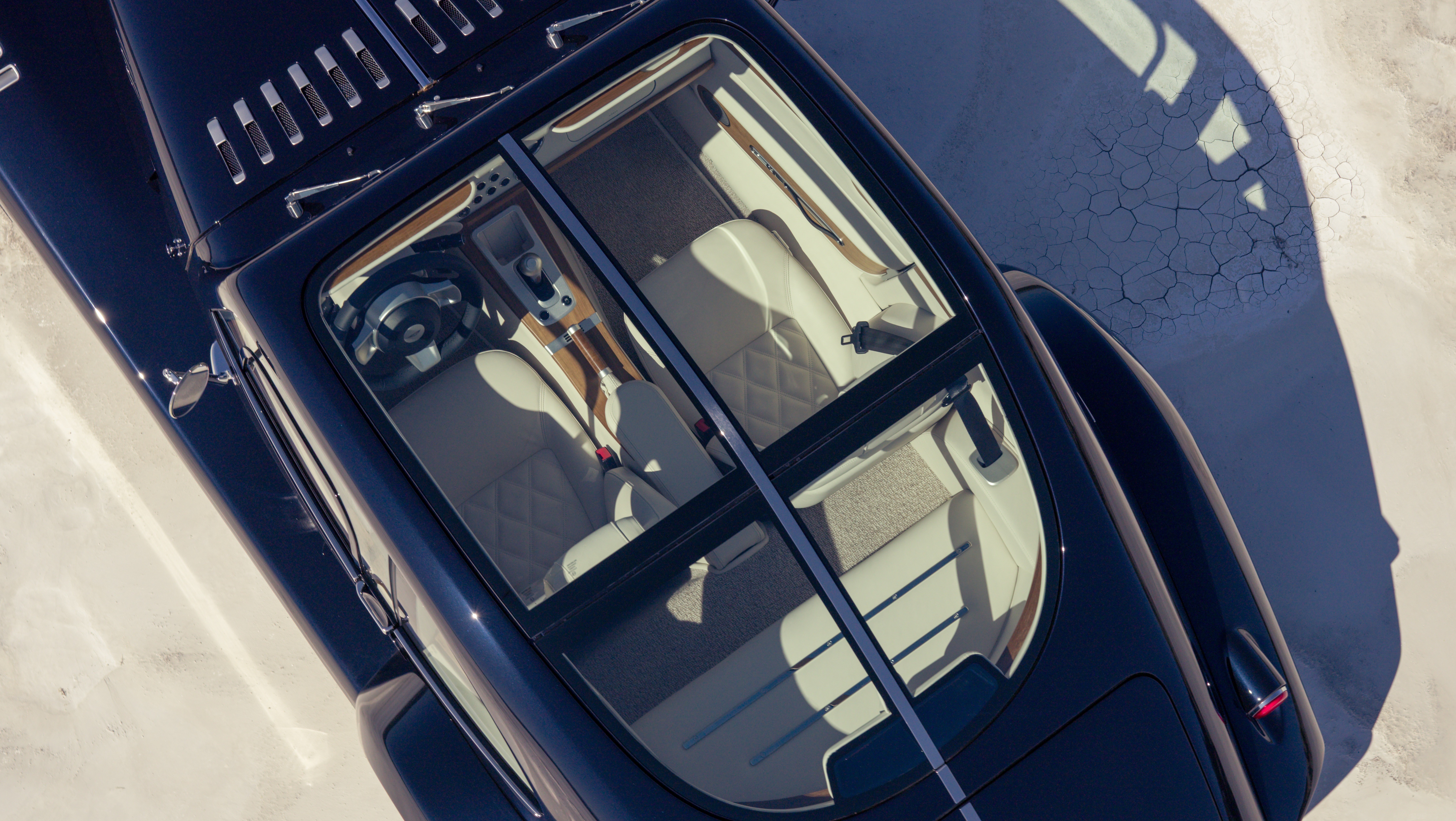 Vista aérea de um carro esportivo azul-marinho com teto solar, interior claro e detalhes em madeira, estacionado em uma superfície clara com sombra projetada e rachaduras no chão