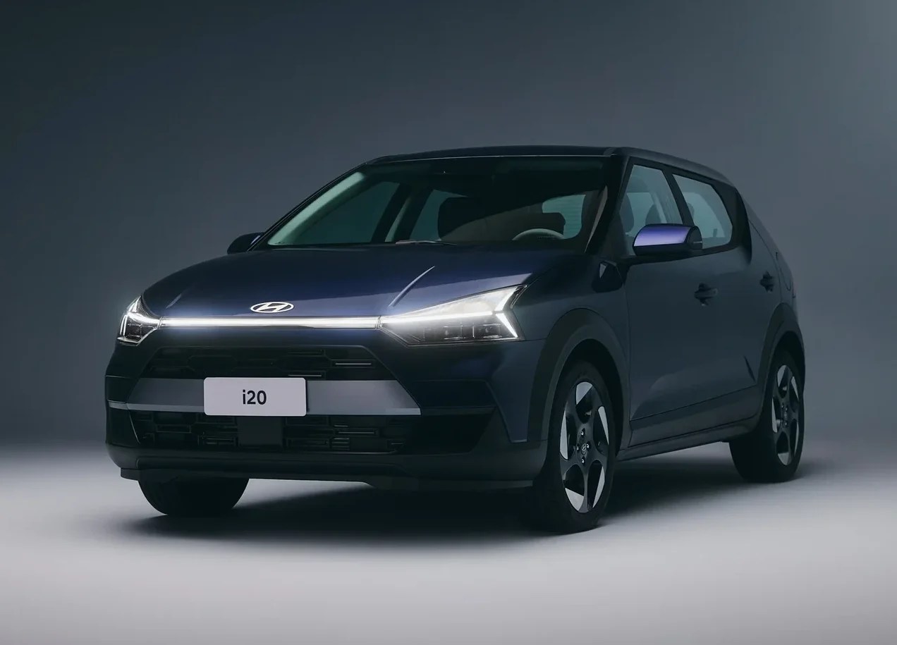 Carro Hyundai i20 azul escuro, com faróis e uma barra de LED horizontal acesos, em estúdio com fundo cinza escuro