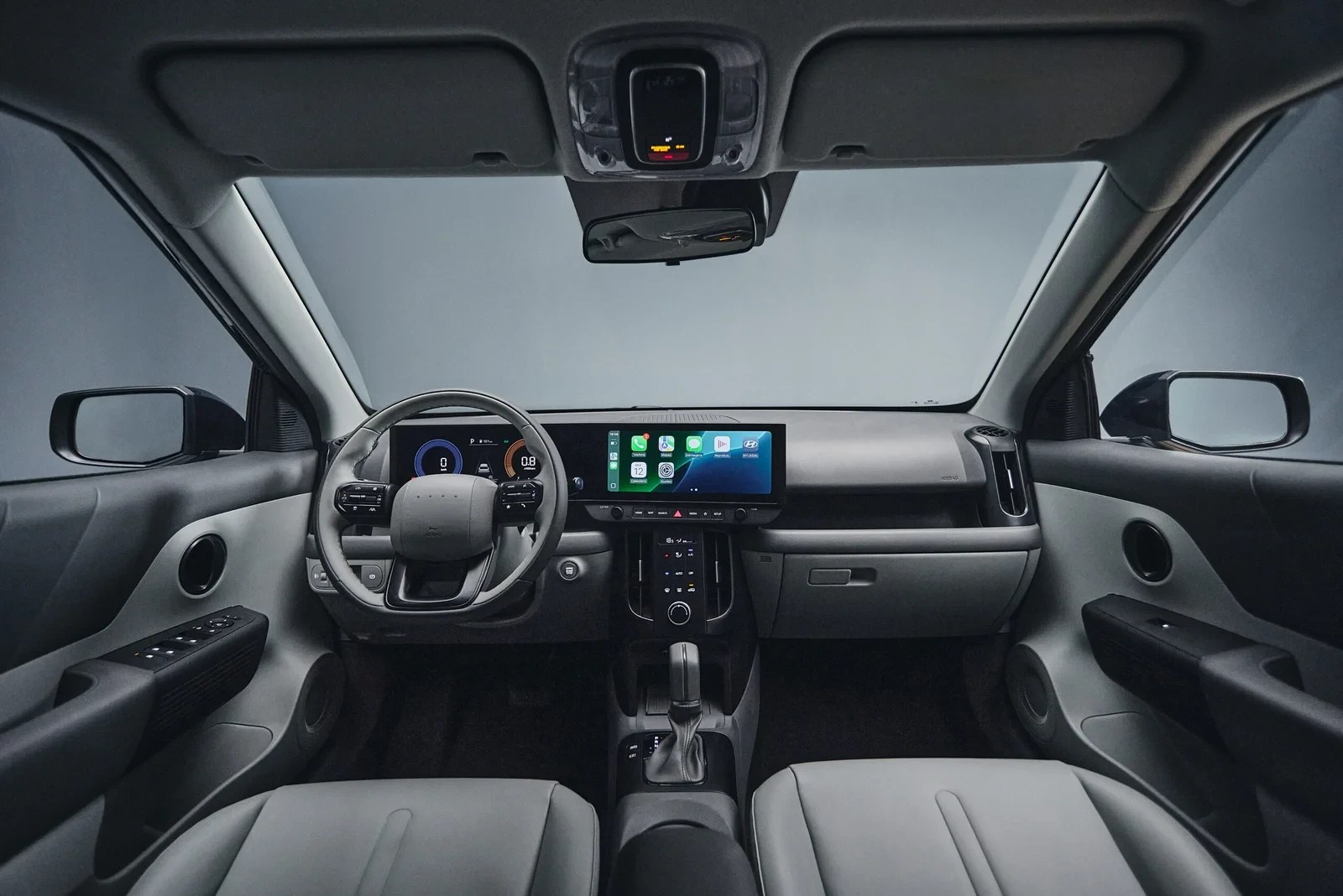 Interior de um carro moderno com painel cinza claro e escuro, volante multifuncional, e duas telas digitais. A tela central exibe ícones de aplicativos, e o banco do motorista é cinza claro com detalhes em branco