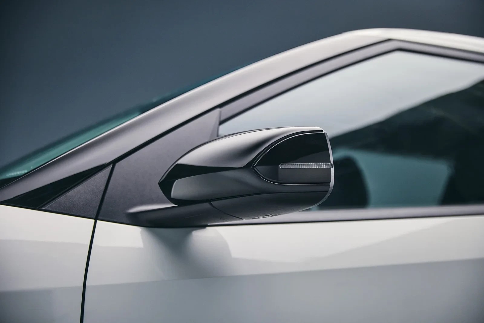 Lateral de um carro branco com retrovisor preto brilhante, detalhe da seta em LED e vidro escuro refletindo o ambiente
