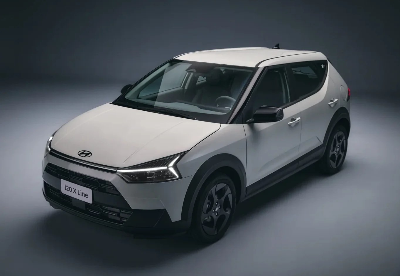 Carro Hyundai i20 X Line branco, visto de cima e ligeiramente de frente, com detalhes pretos nos para-lamas e rodas, em um estúdio cinza escuro
