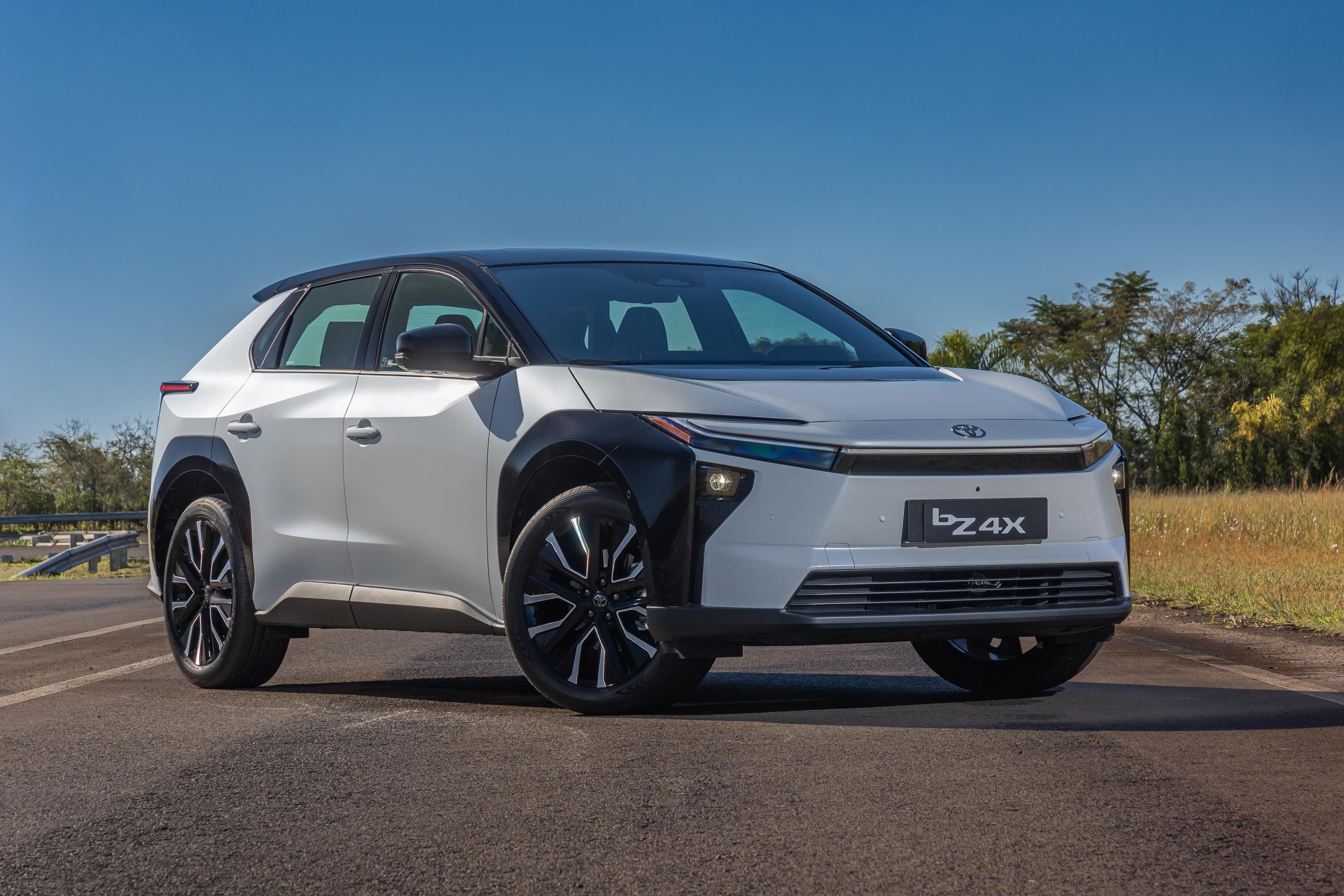 SUV elétrico Toyota bZ4X branco e preto, estacionado em uma estrada asfaltada, com vegetação e céu azul ao fundo