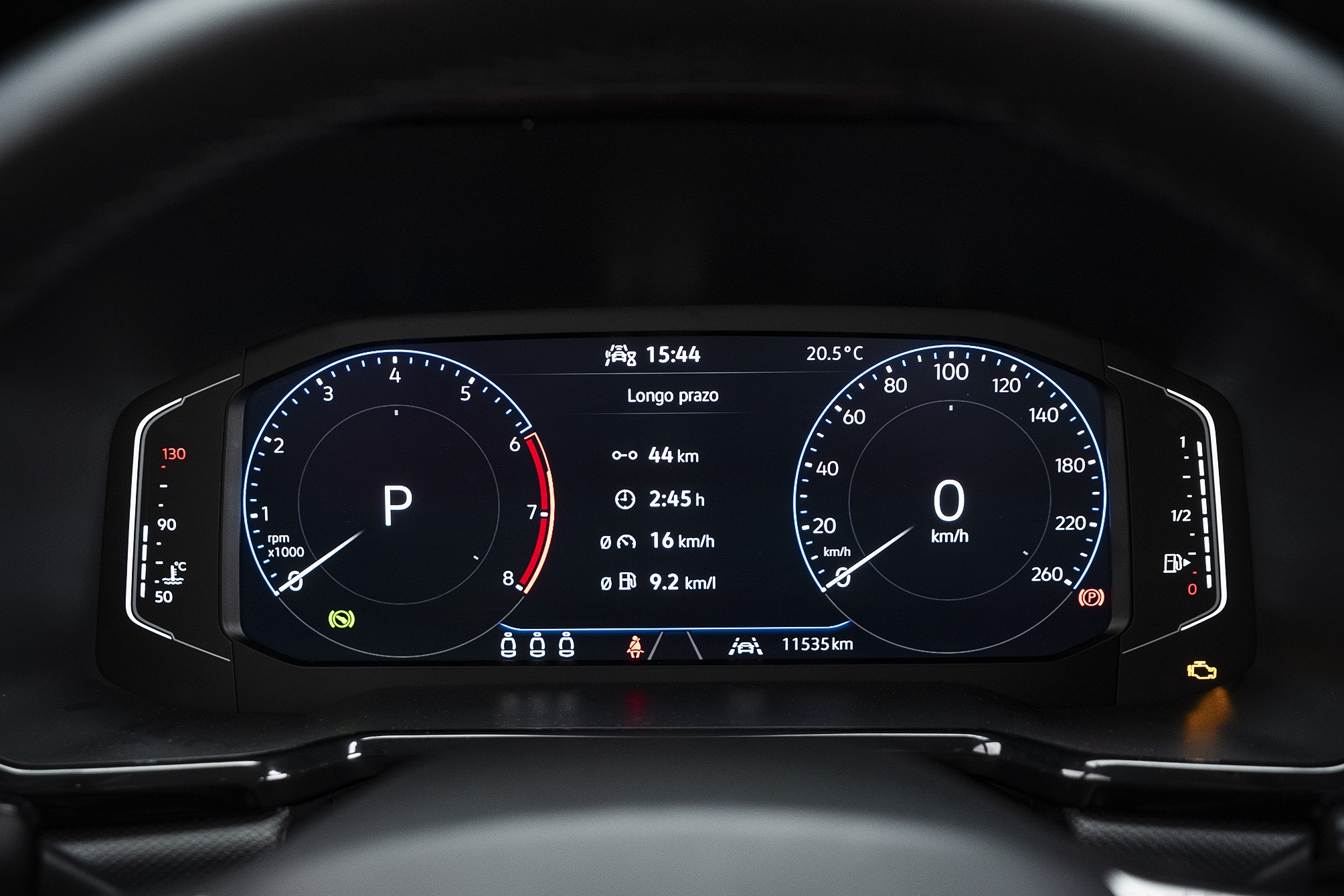 Painel digital de carro com velocímetro marcando 0 km/h e conta-giros em P. Exibe 15:44, temperatura de 20.5°C, 44 km percorridos, 2:45h de viagem, consumo de 16 km/h e 9.2 km/l, além de 11535 km totais. Luzes de advertência acesas no canto inferior direito