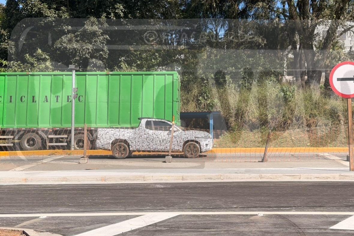Caminhão verde com a palavra CICLATEC e uma picape camuflada estacionados em uma rua, com uma placa de sentido único apontando para a direita