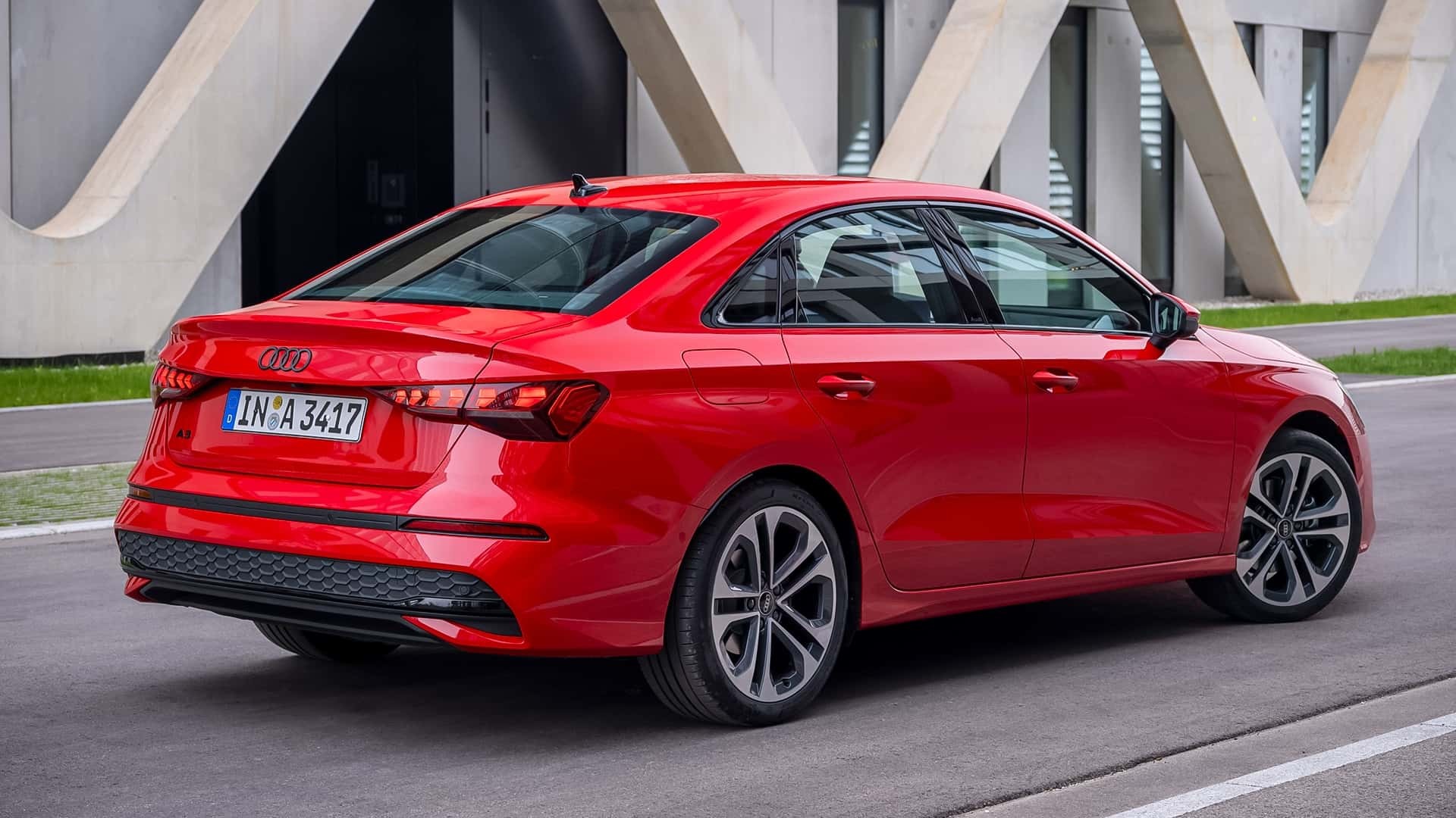Carro Audi A3 Sedan vermelho estacionado em uma rua, visto de traseira e lateral, com um prédio moderno de concreto ao fundo
